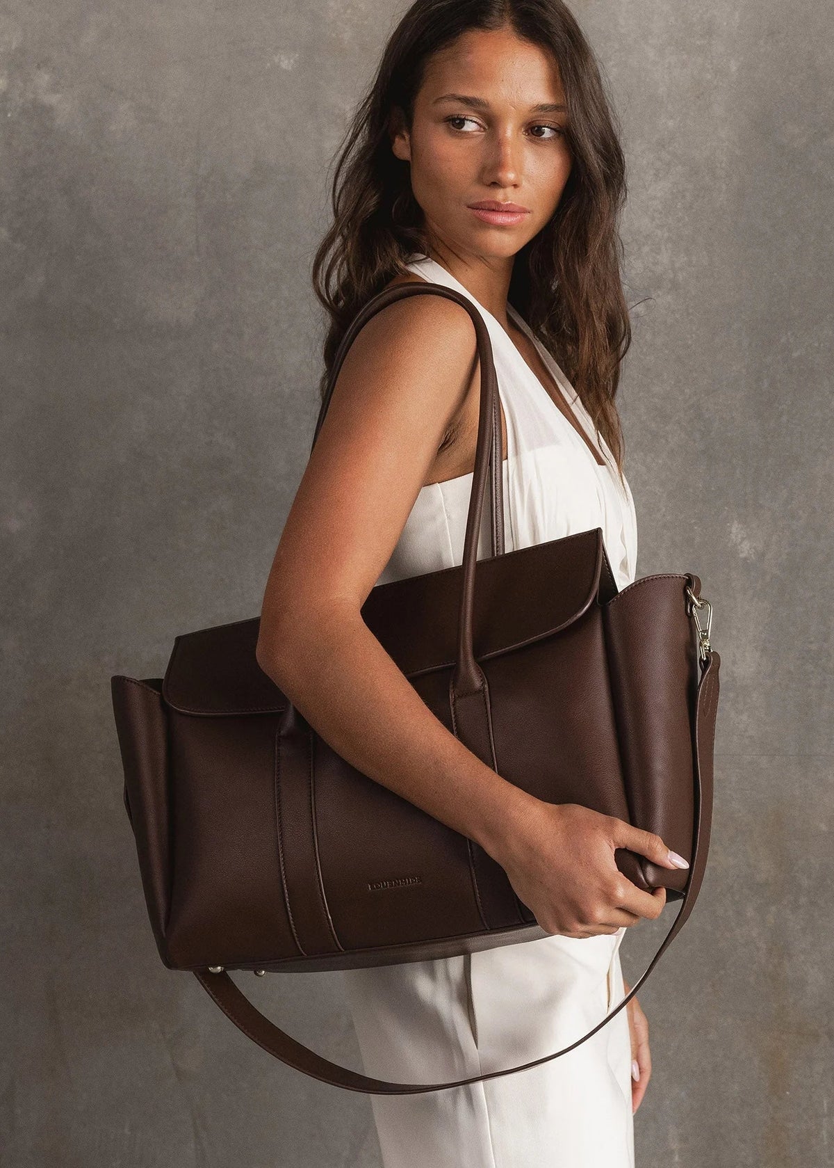 Woman holding a brown leather handbag against a gray background