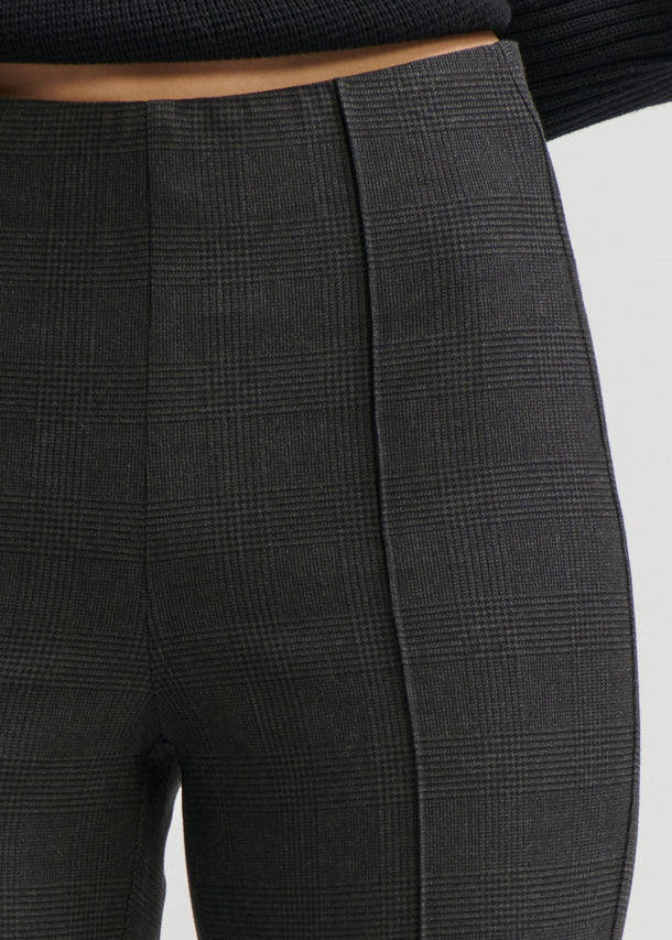 Close-up of a person wearing dark charcoal gray plaid trousers, showing the waistband, front seam, and thigh area against a light gray background.