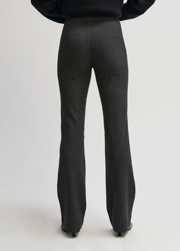 Rear view of a person wearing dark charcoal flared trousers and a black top against a light gray studio background.
