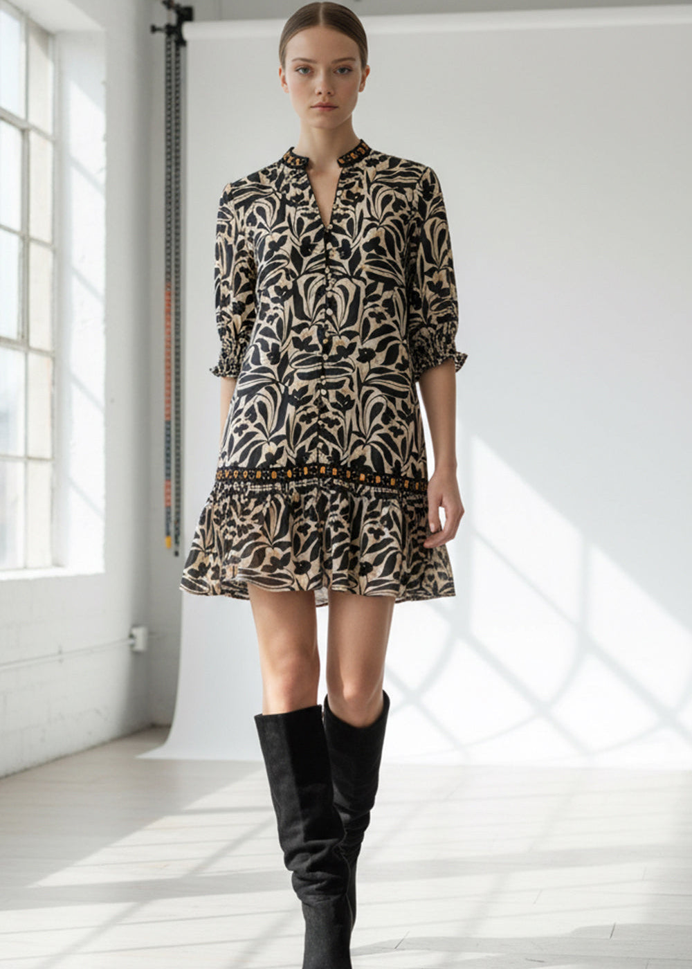 Woman wearing a patterned dress and black knee-high boots in a bright room.