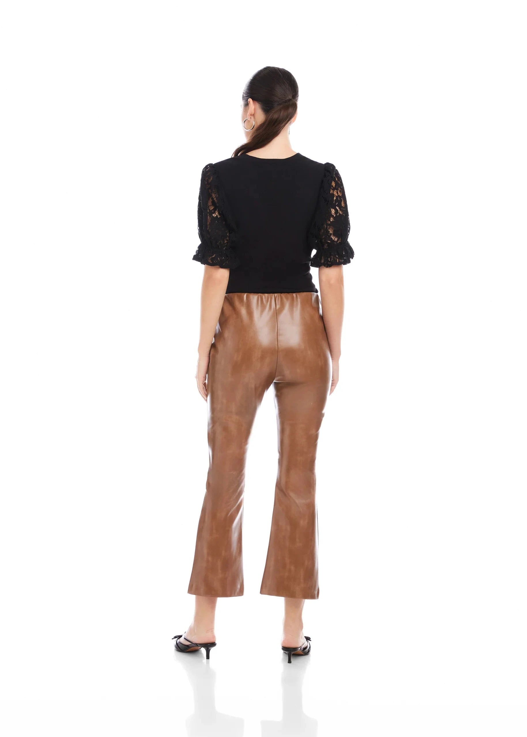 Woman wearing a black top with lace sleeves and brown pants on a white background