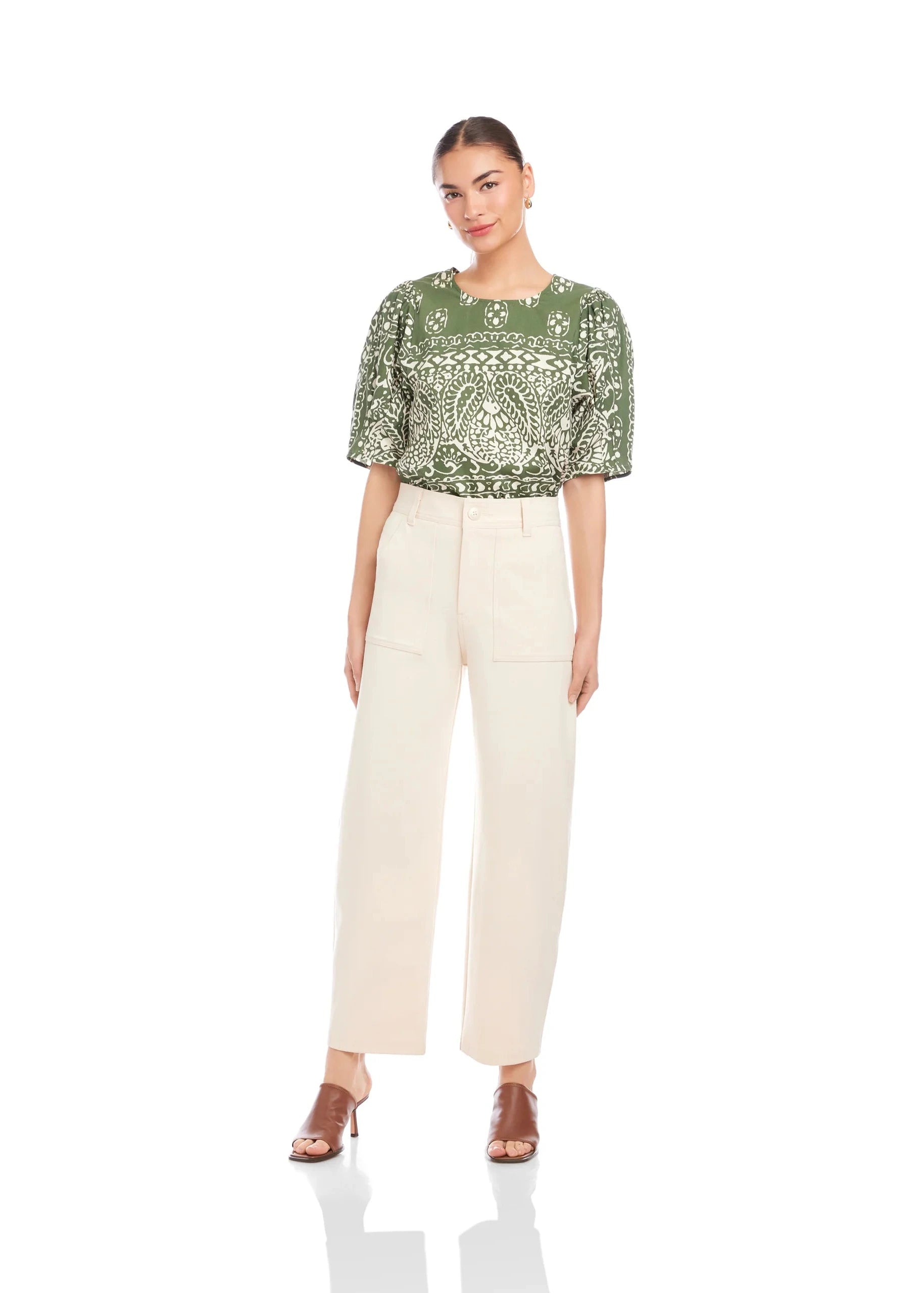 Woman wearing a green patterned top and beige pants on a white background