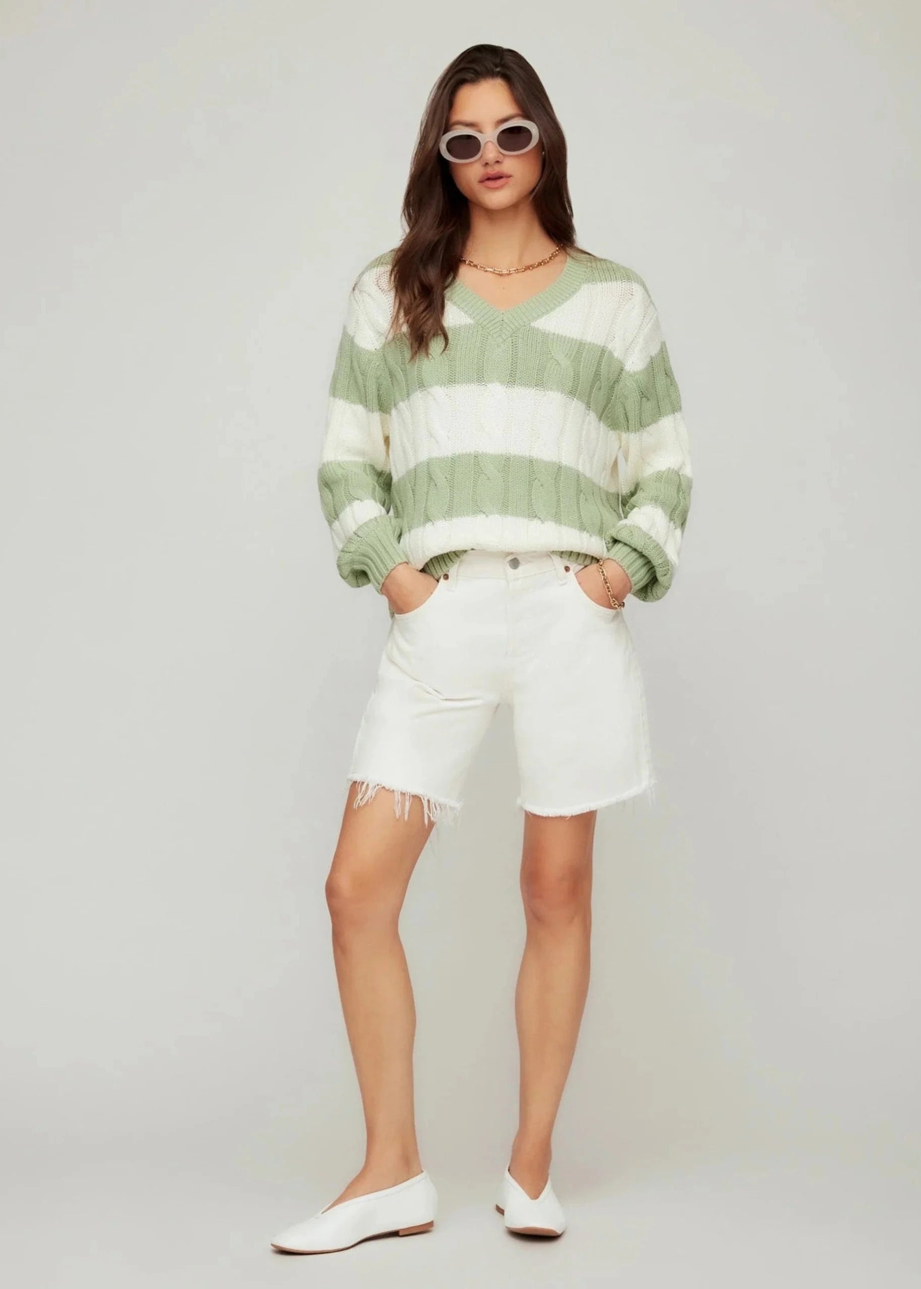 Woman wearing a green and white striped sweater and white shorts on a plain background