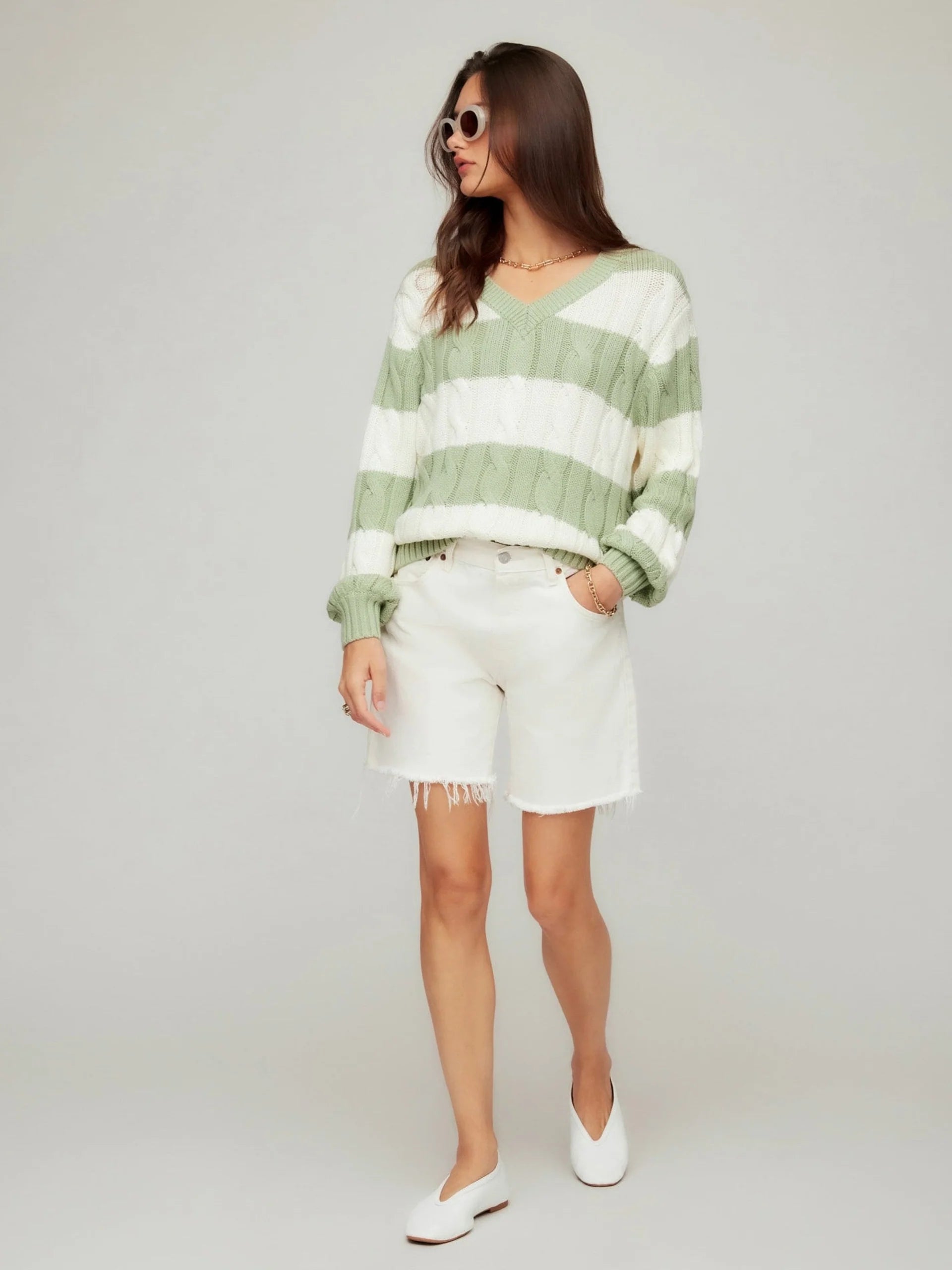 Woman wearing a green and white striped sweater with white shorts on a plain background