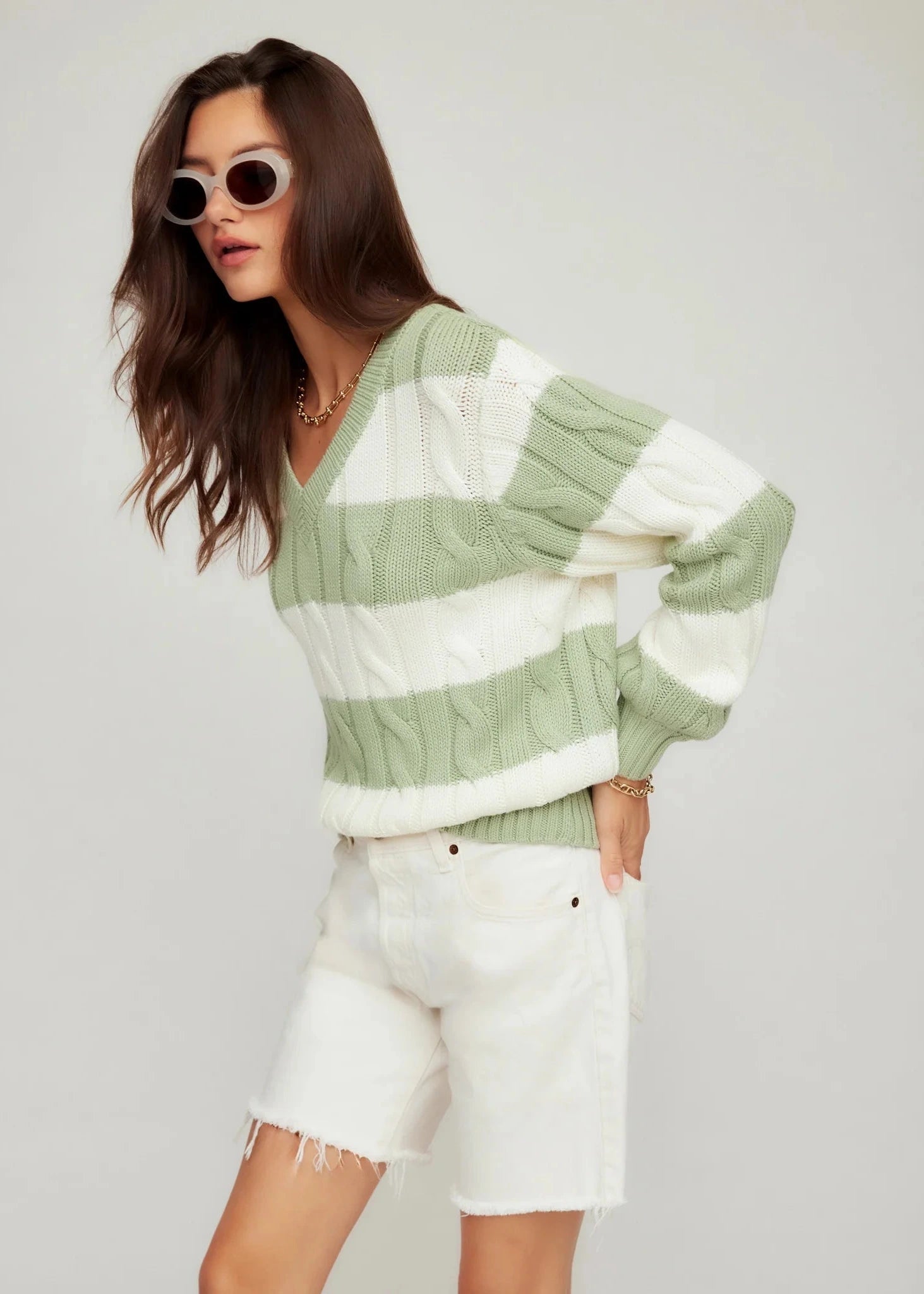 Woman wearing a green and white striped sweater with white shorts on a plain background