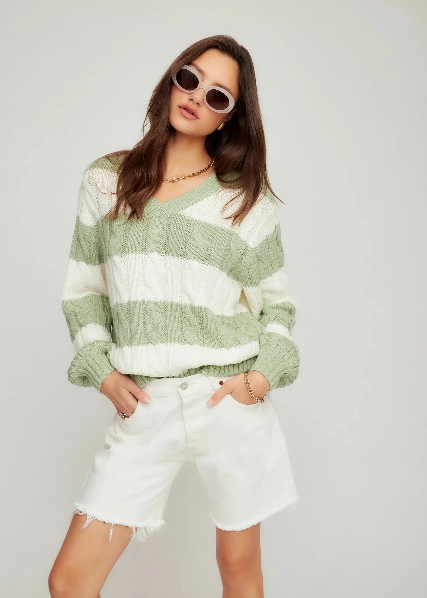 Woman wearing a green and white striped sweater with white shorts on a plain background