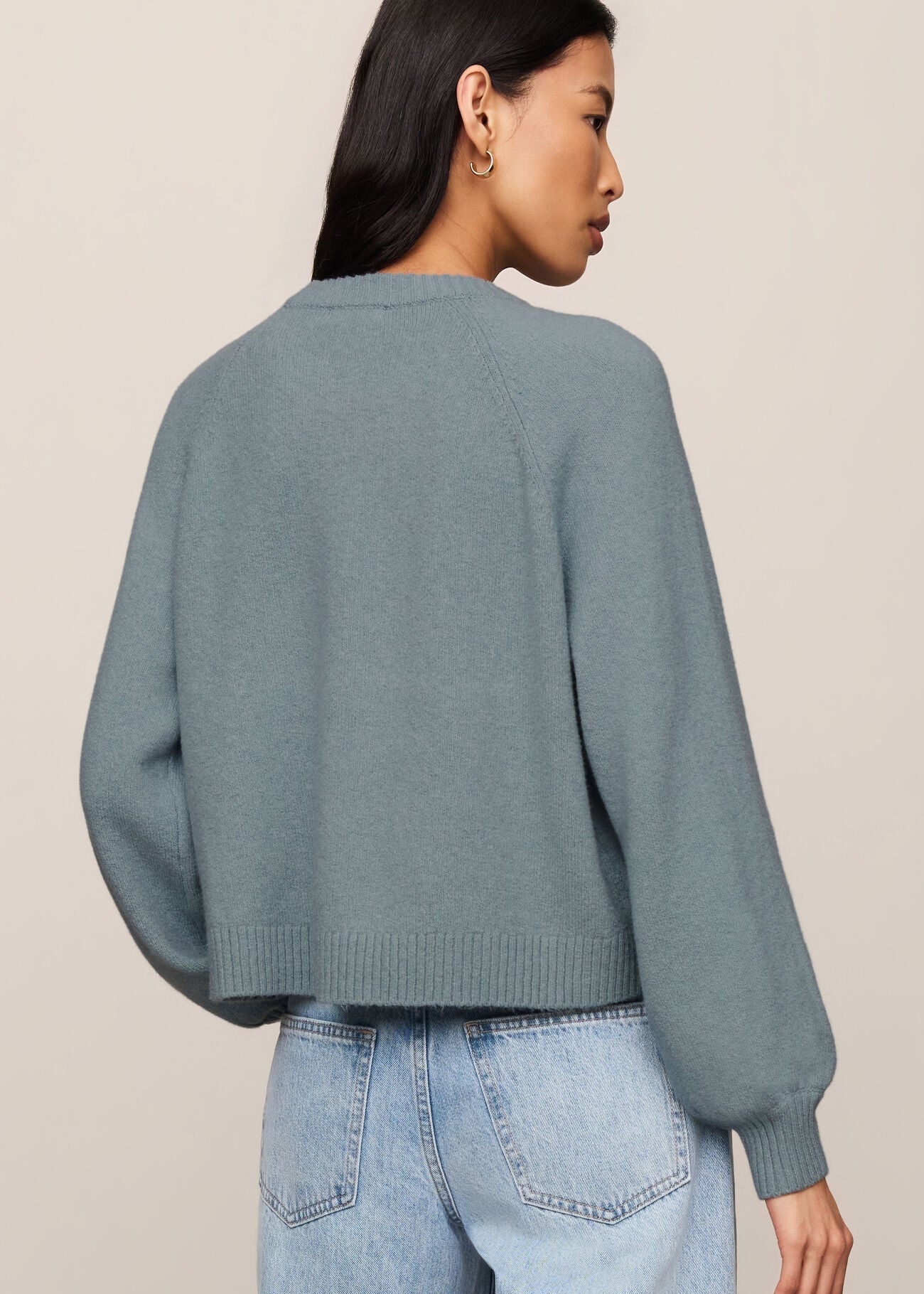 Person wearing a light blue sweater and jeans on a beige background
