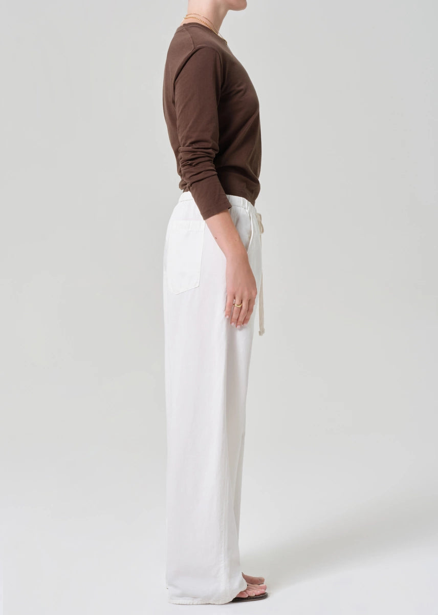 Person wearing a brown top and white pants on a plain background