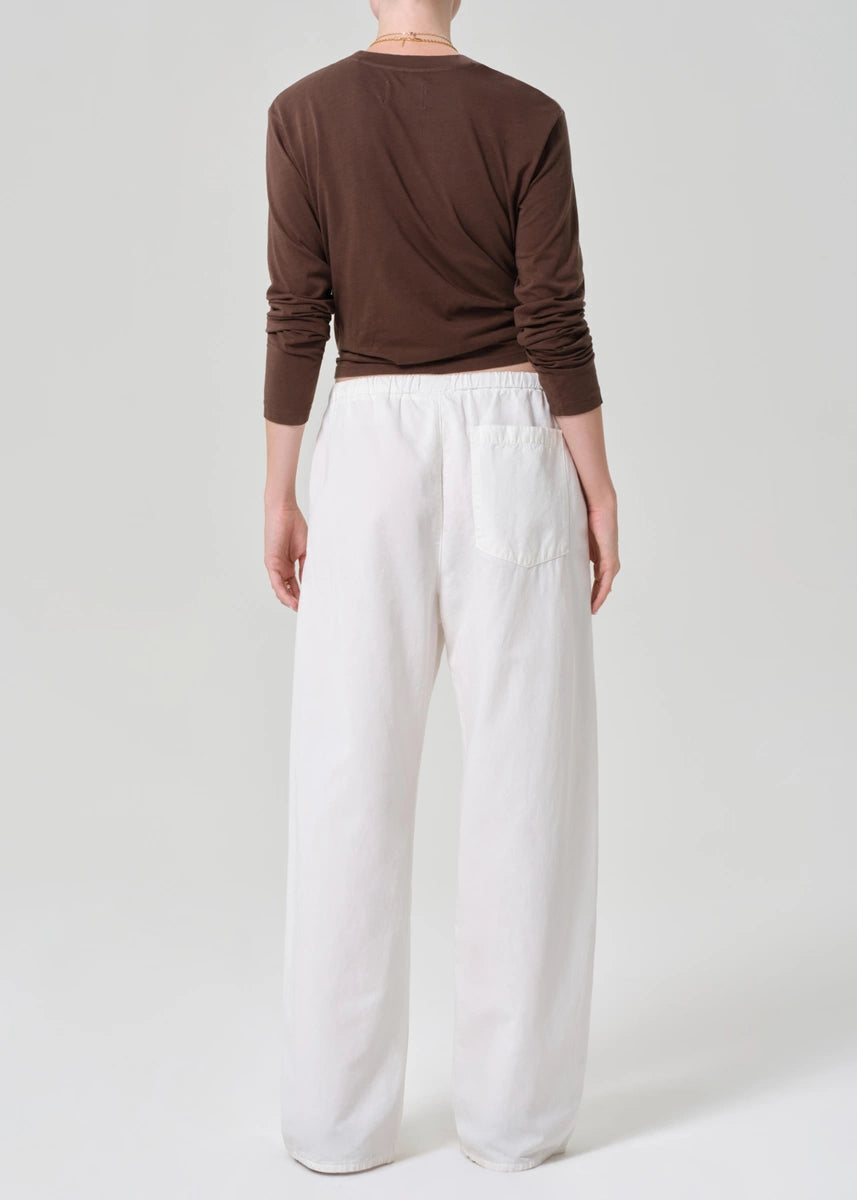 Person wearing a brown long-sleeve top and white wide-leg pants on a plain background