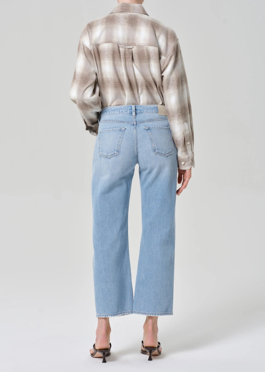 Person wearing a patterned shirt and light blue jeans on a plain background