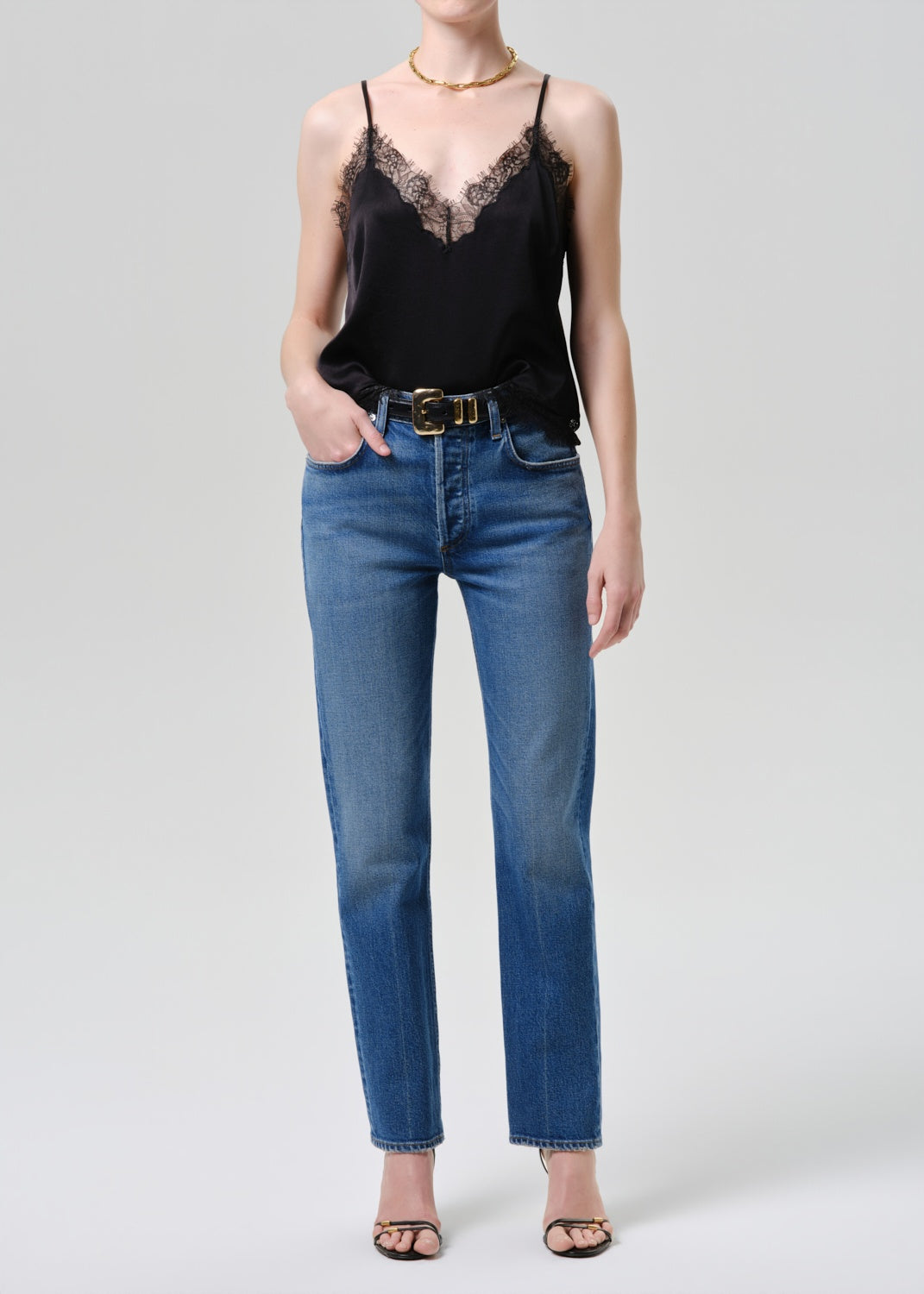 Person wearing a black lace top and blue jeans on a white background