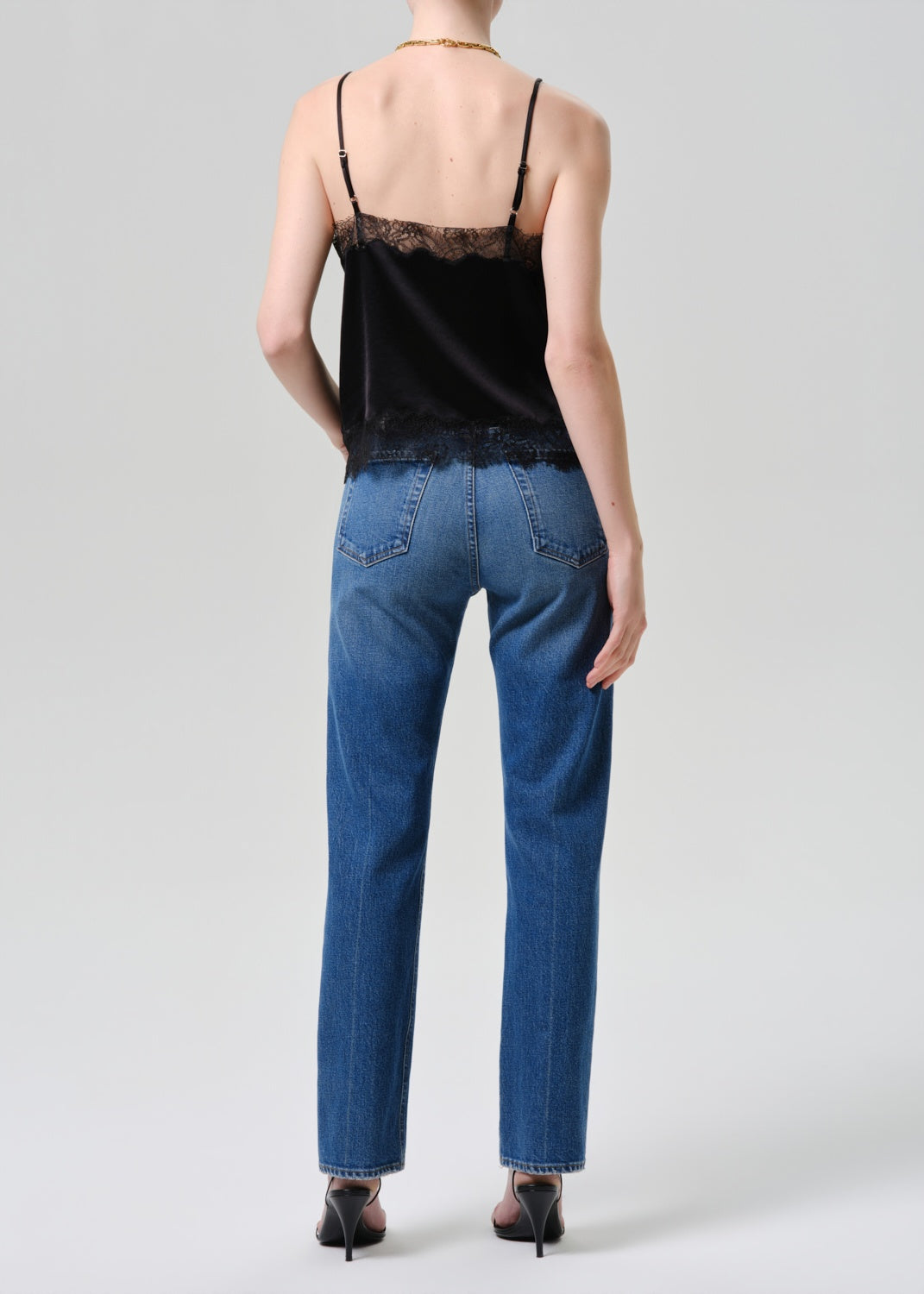 Person wearing a black lace top and blue jeans on a white background