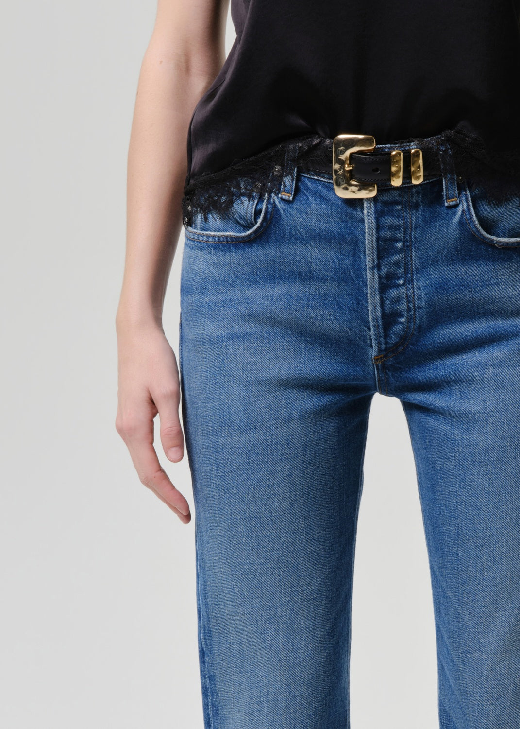 Person wearing blue jeans with a gold belt on a plain background