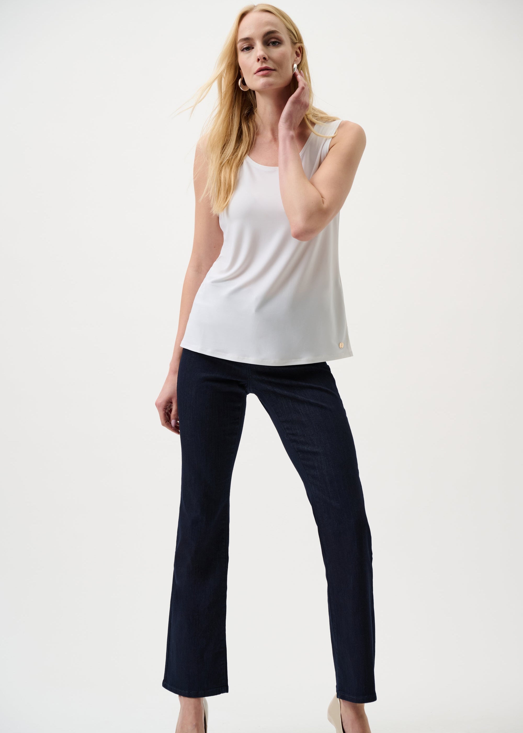 Woman wearing a white sleeveless top and dark pants on a white background