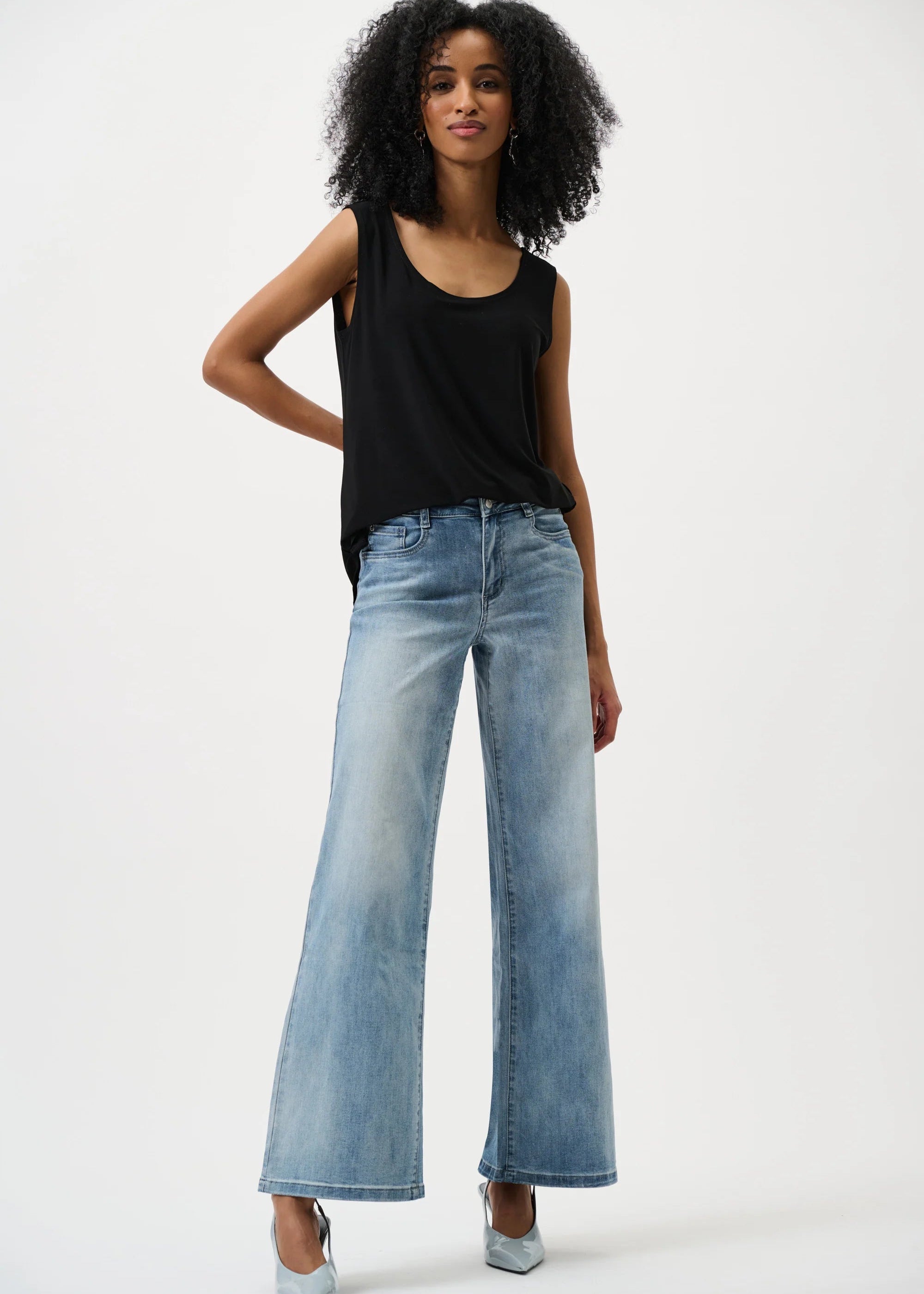 A woman modeling a black sleeveless top and light blue wide-leg denim jeans against a plain white studio background.