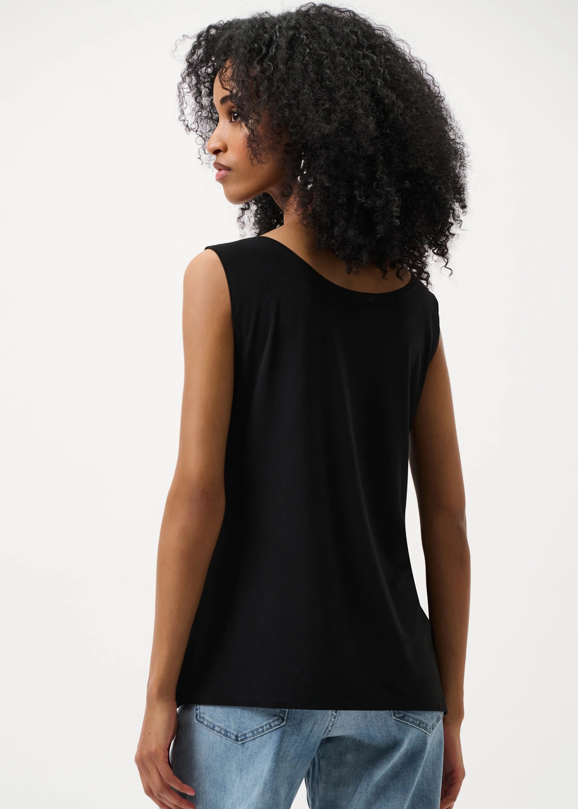 Woman wearing a black sleeveless top and light blue jeans on a white background