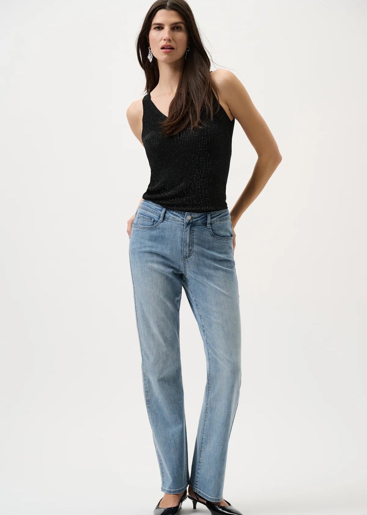 Woman wearing a black sleeveless top and light blue jeans on a white background