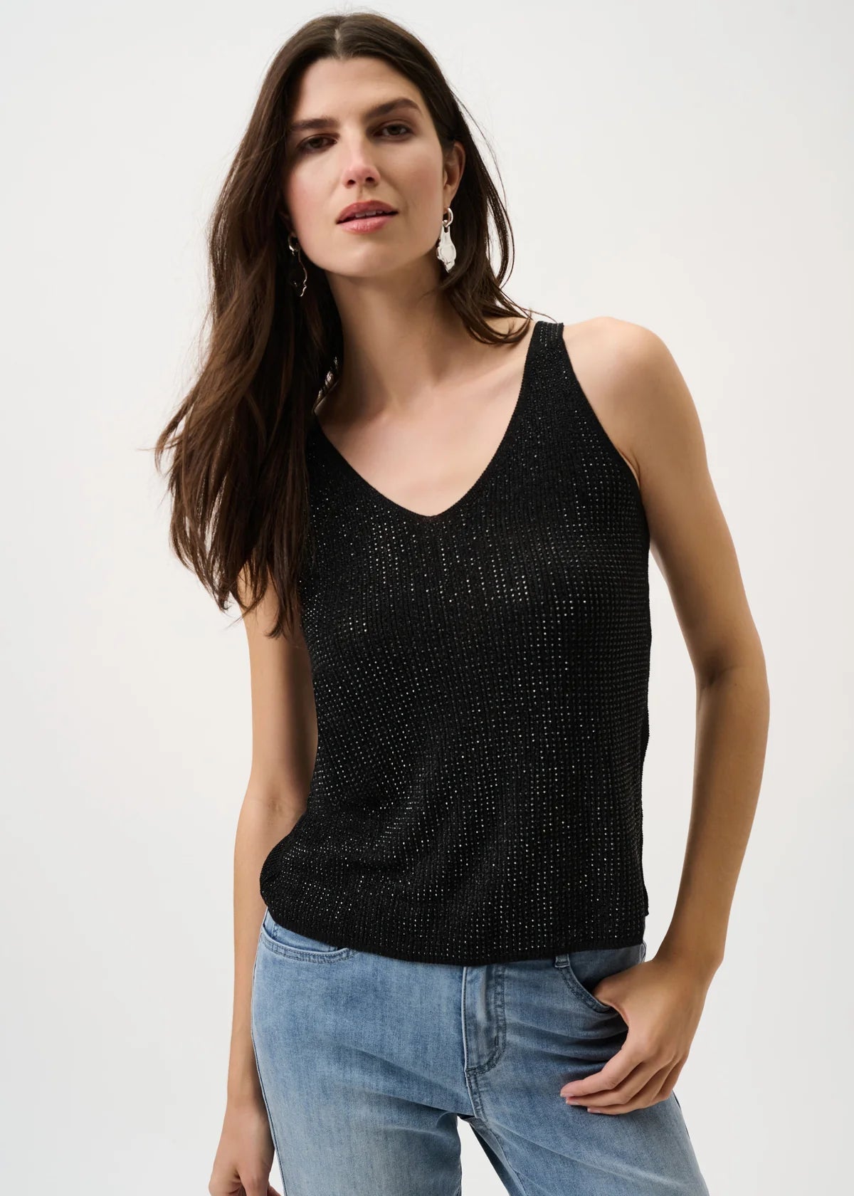 Woman wearing a black tank top and blue jeans on a white background