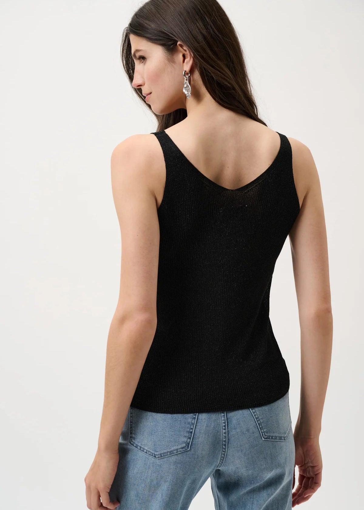 Woman wearing a black tank top and blue jeans on a white background