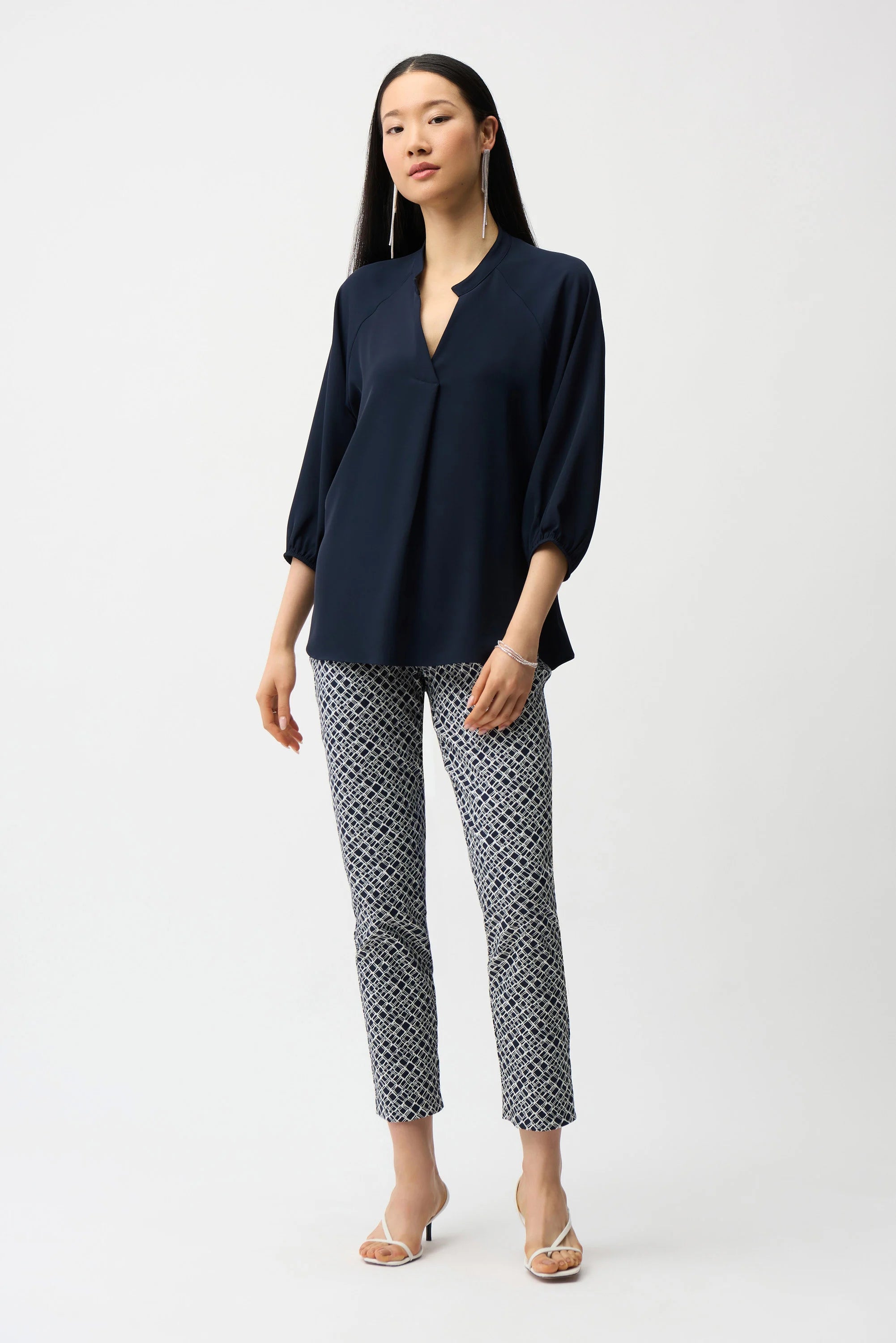 Woman wearing a navy blue blouse and patterned pants on a white background