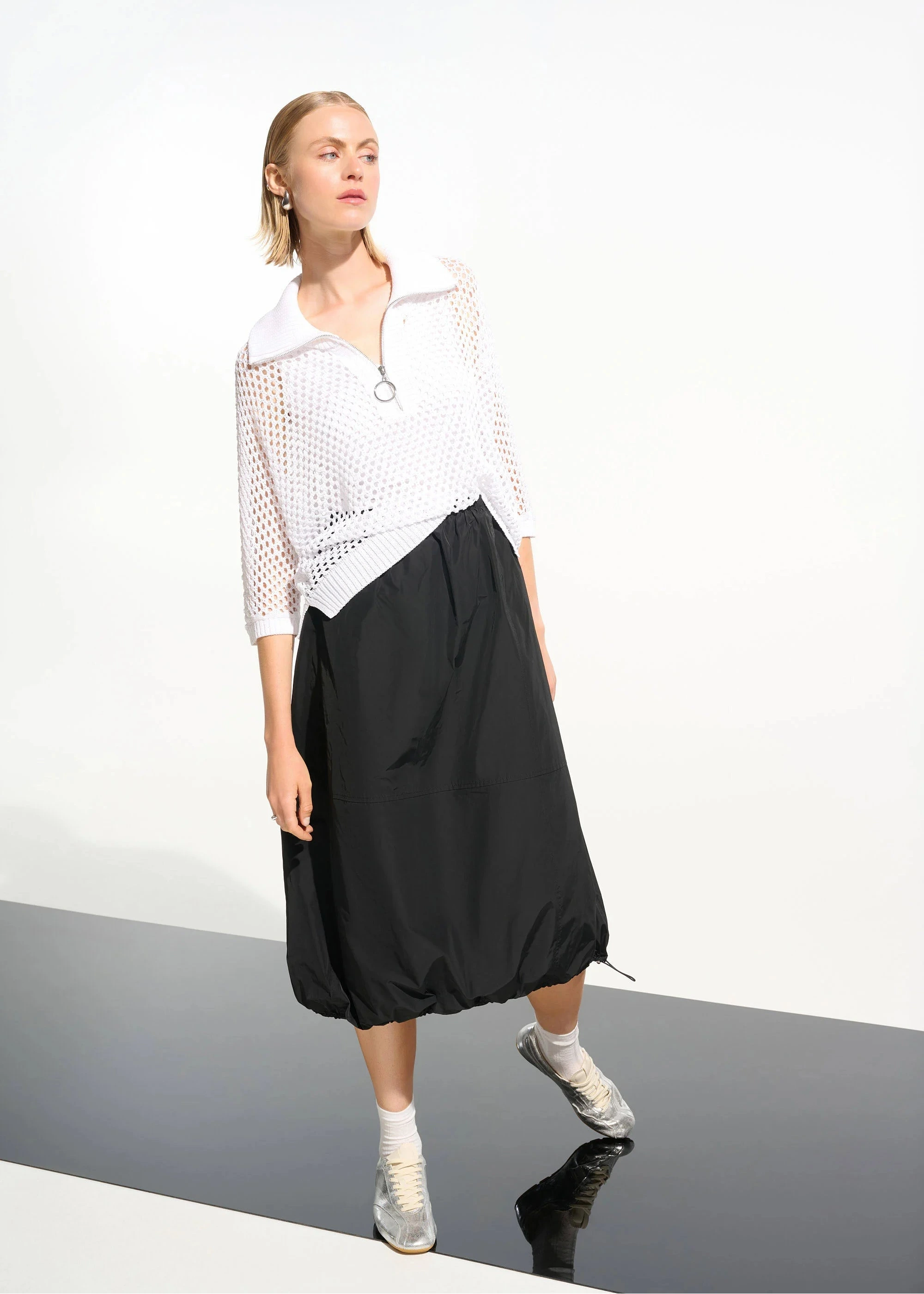 Person wearing a white top and black skirt on a plain background