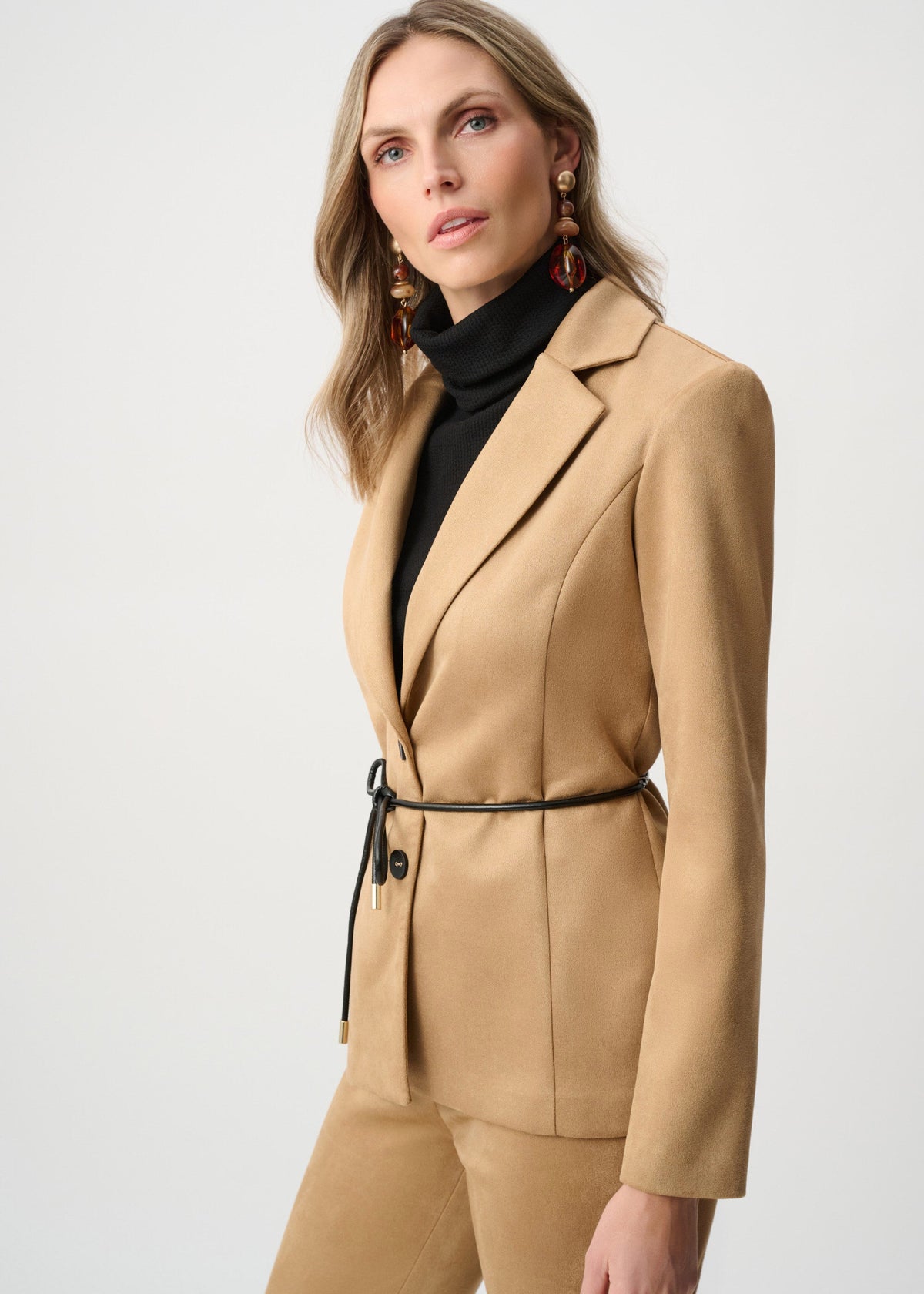 Woman wearing a beige suit with a black turtleneck on a white background