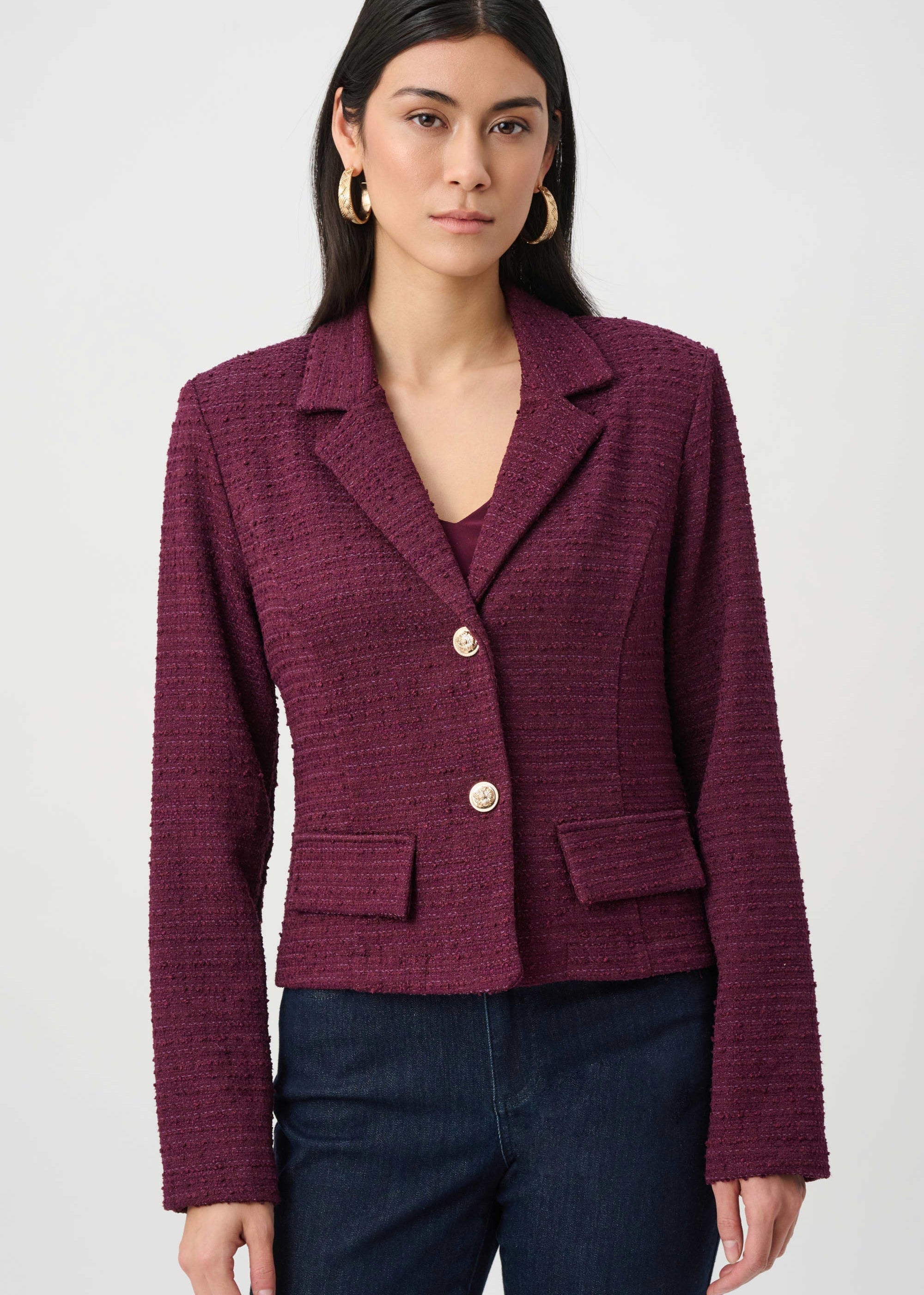 Woman wearing a burgundy blazer with gold buttons on a white background
