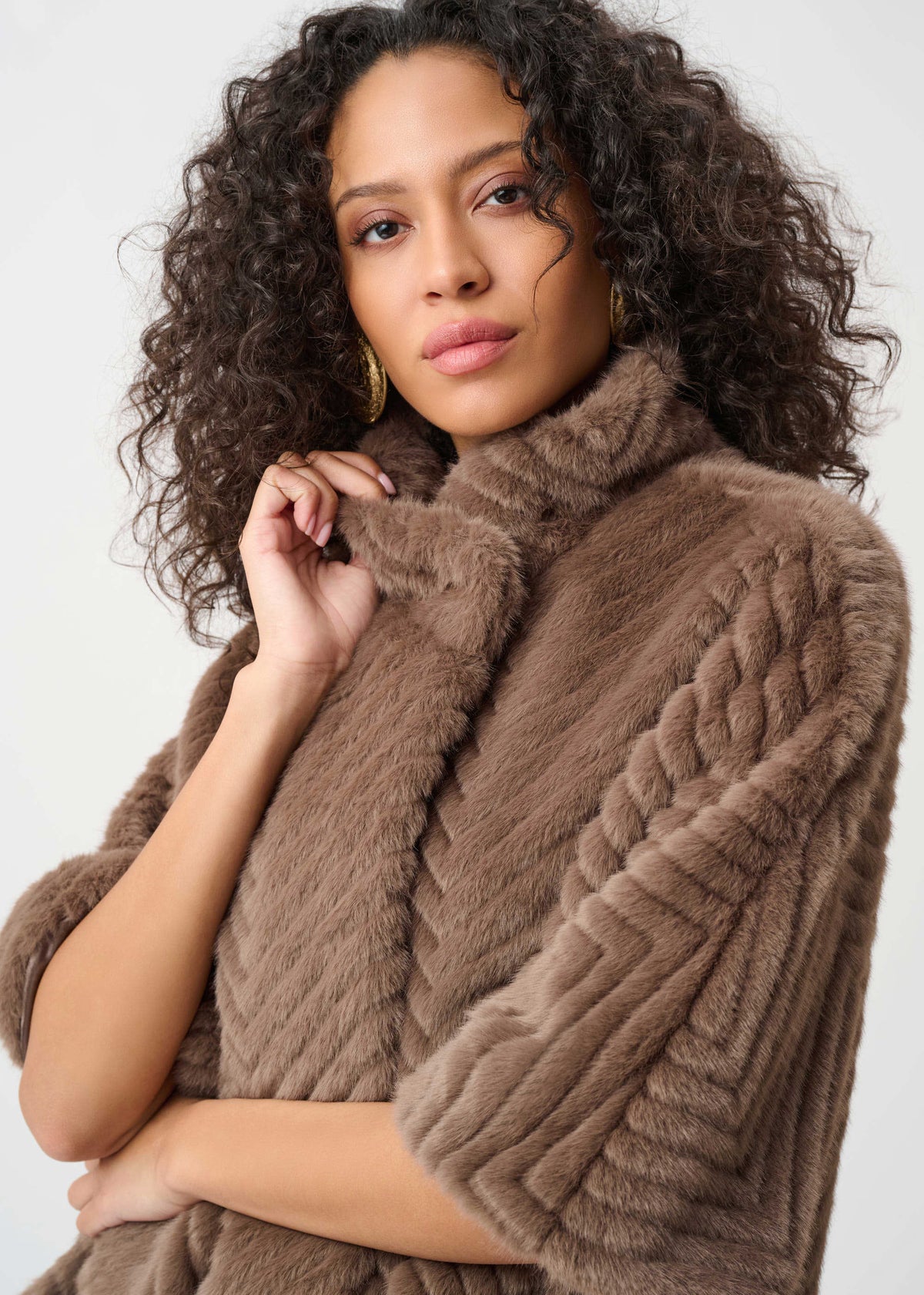 Woman wearing a brown cable knit poncho against a plain background