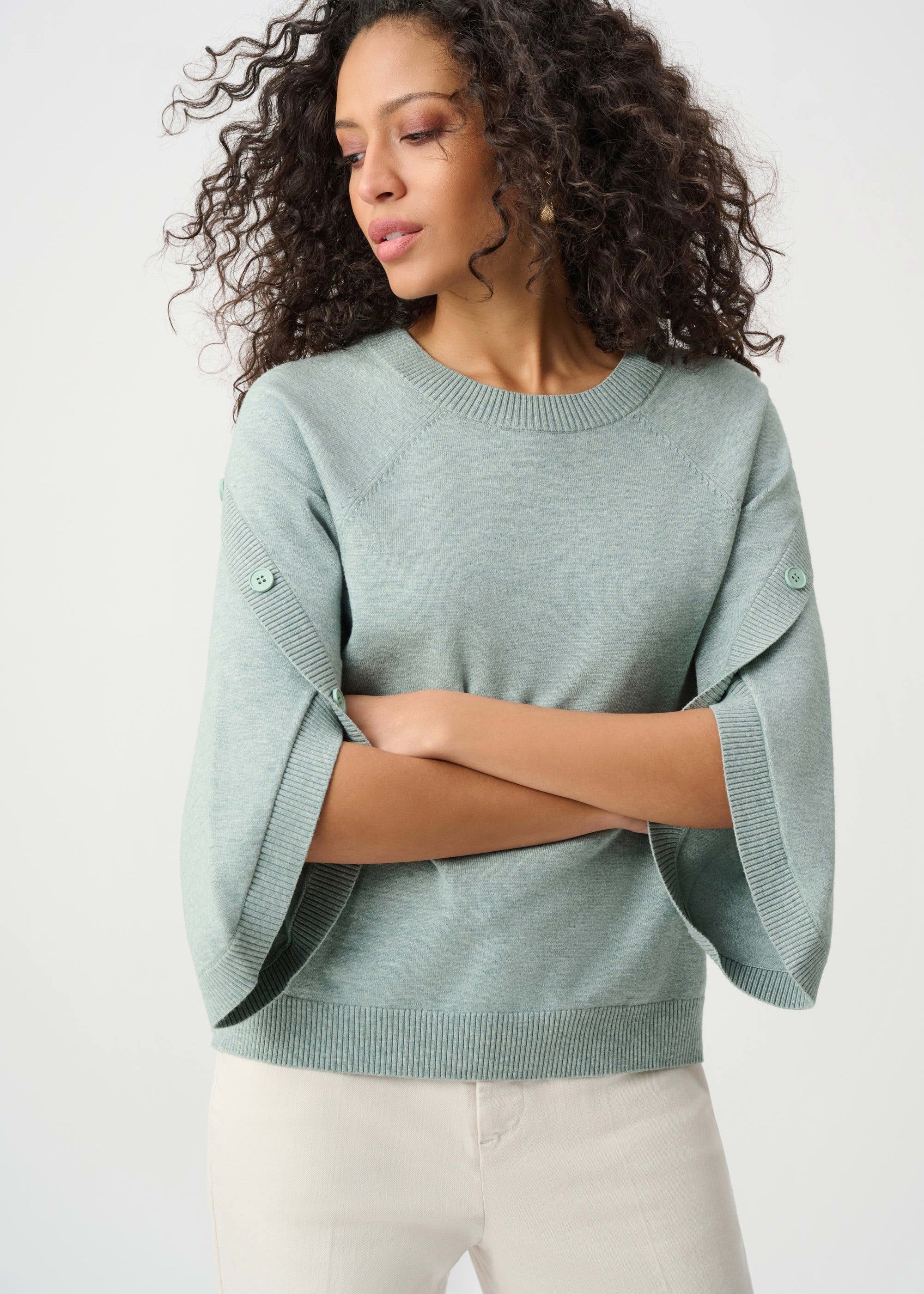 Woman wearing a light green sweater with bell sleeves against a white background