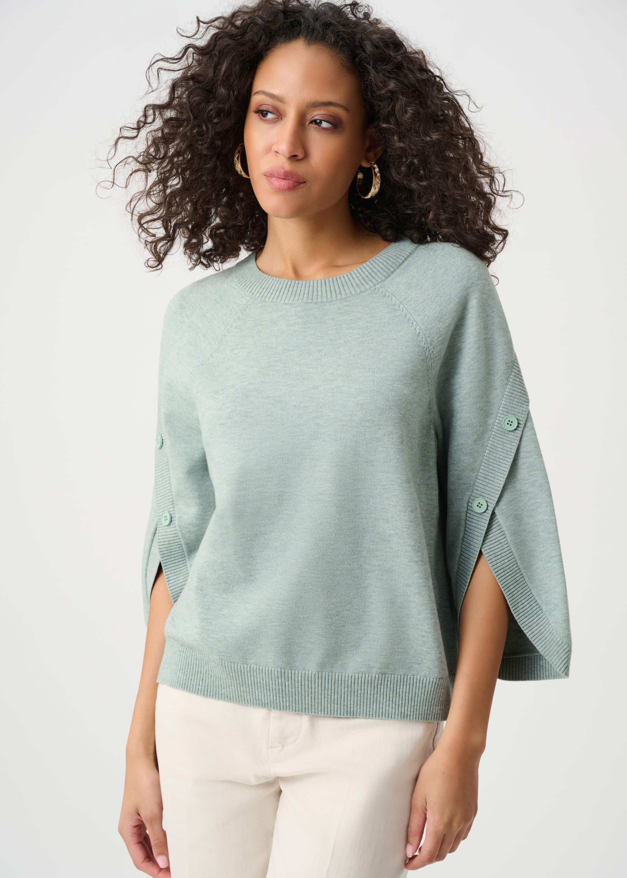 Woman wearing a light green poncho over a white top on a plain background