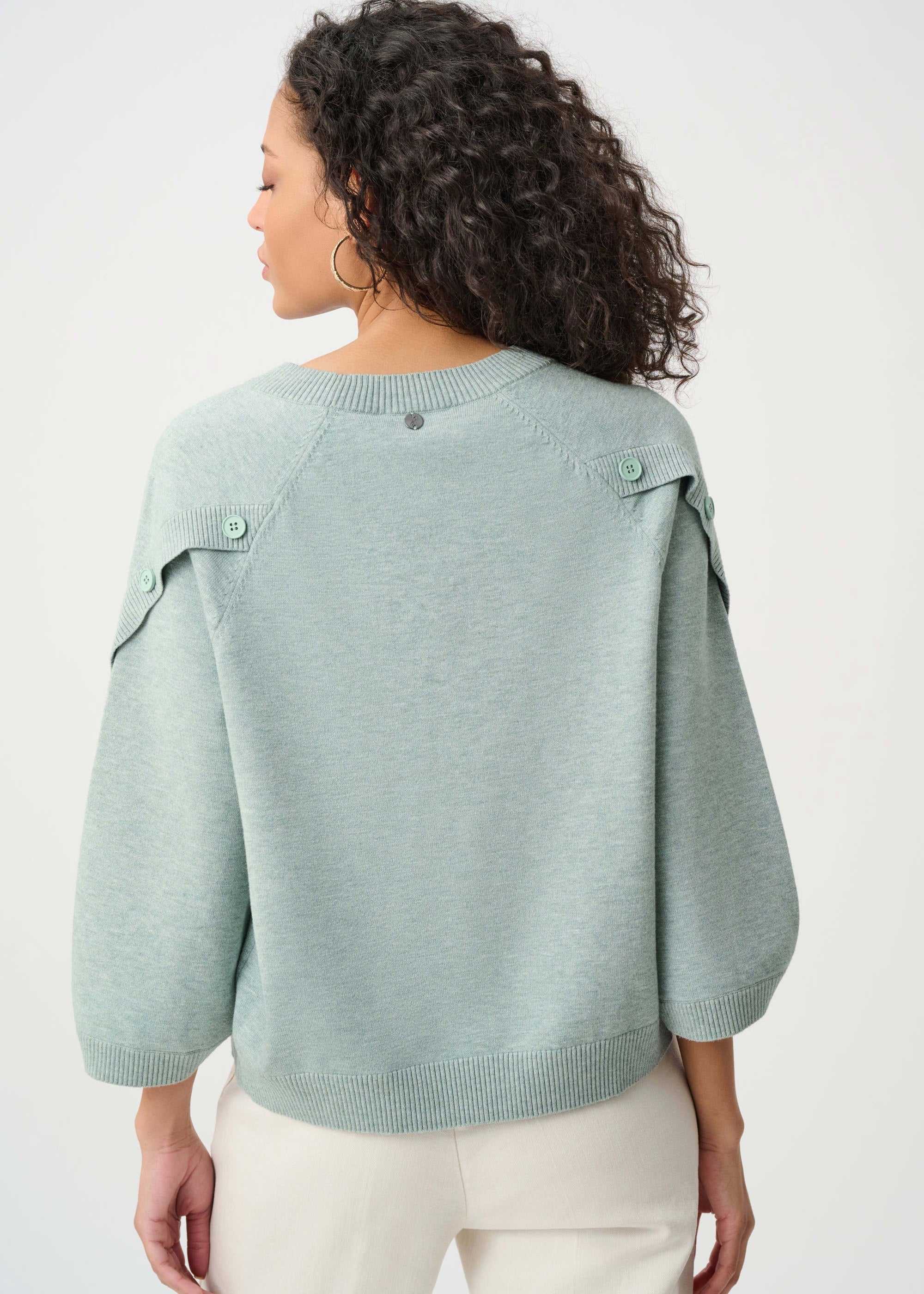 Woman wearing a light green sweater with button details on a white background