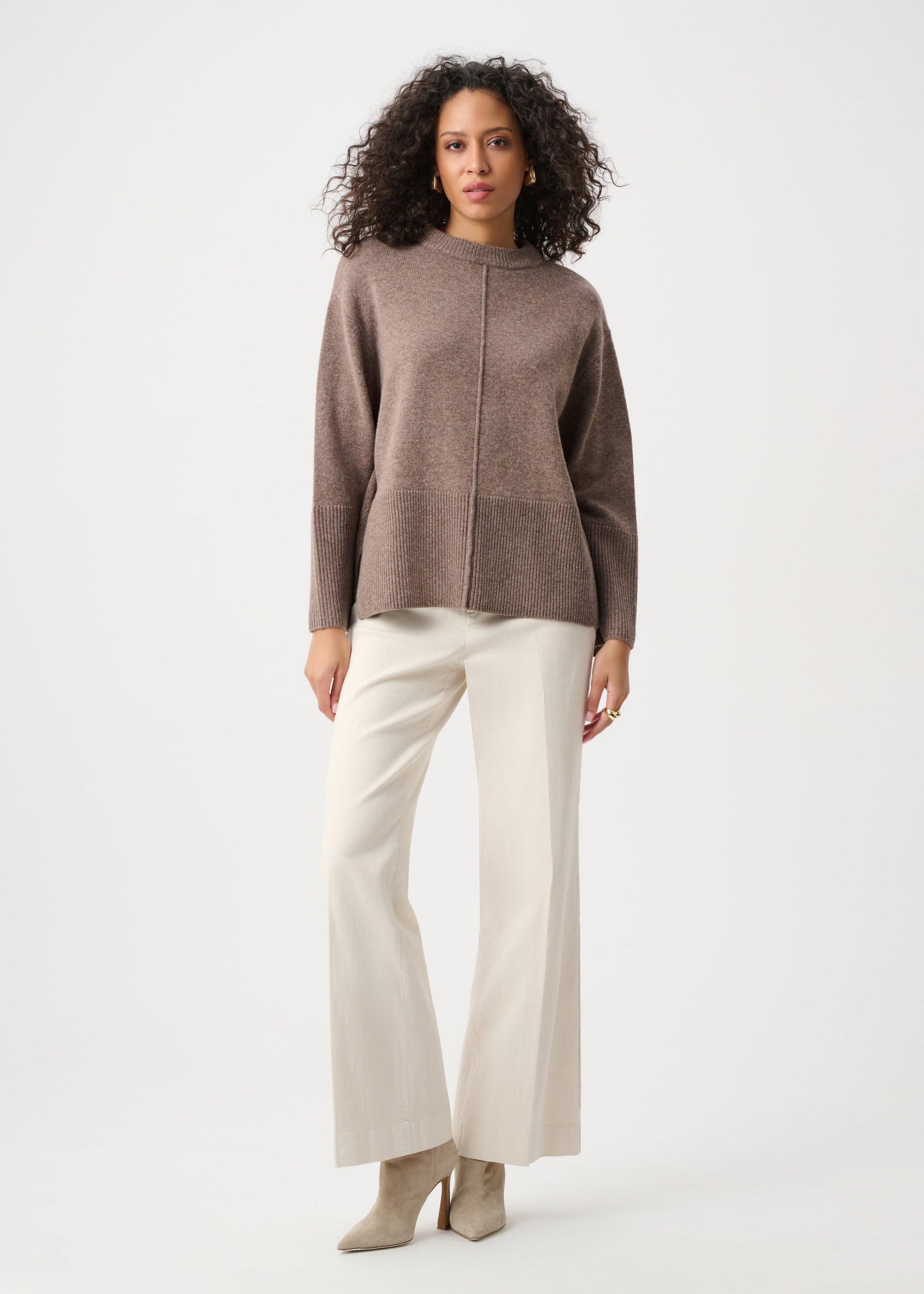 Woman wearing a brown sweater and white pants on a white background
