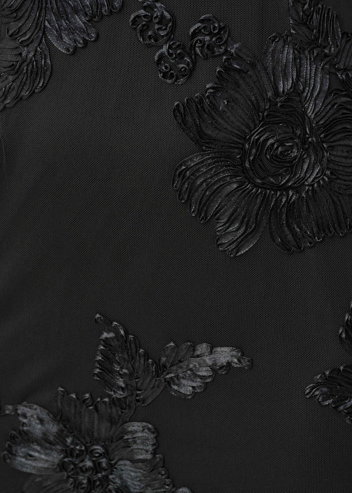 Close-up of a black fabric surface with large raised floral embroidery or applique in matching black and very dark charcoal tones.