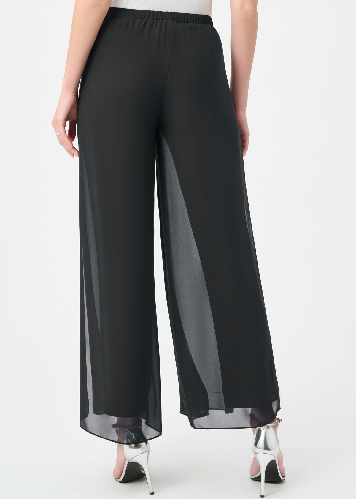Black wide-leg sheer chiffon pants shown from the back on a model, paired with silver high-heeled sandals against a plain white studio background.