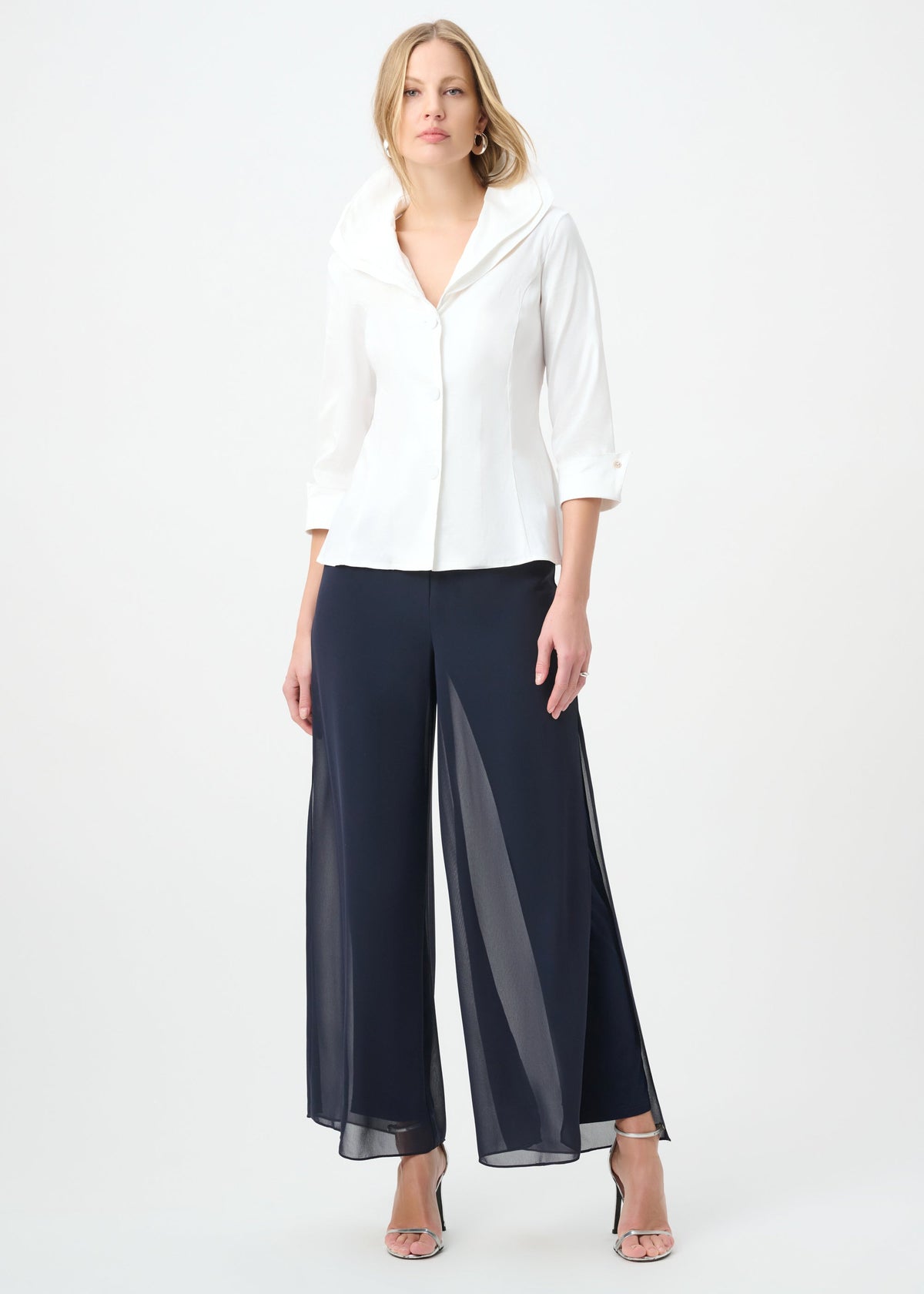 A woman modeling a white long-sleeve collared blouse and navy wide-leg sheer pants against a plain white studio background.
