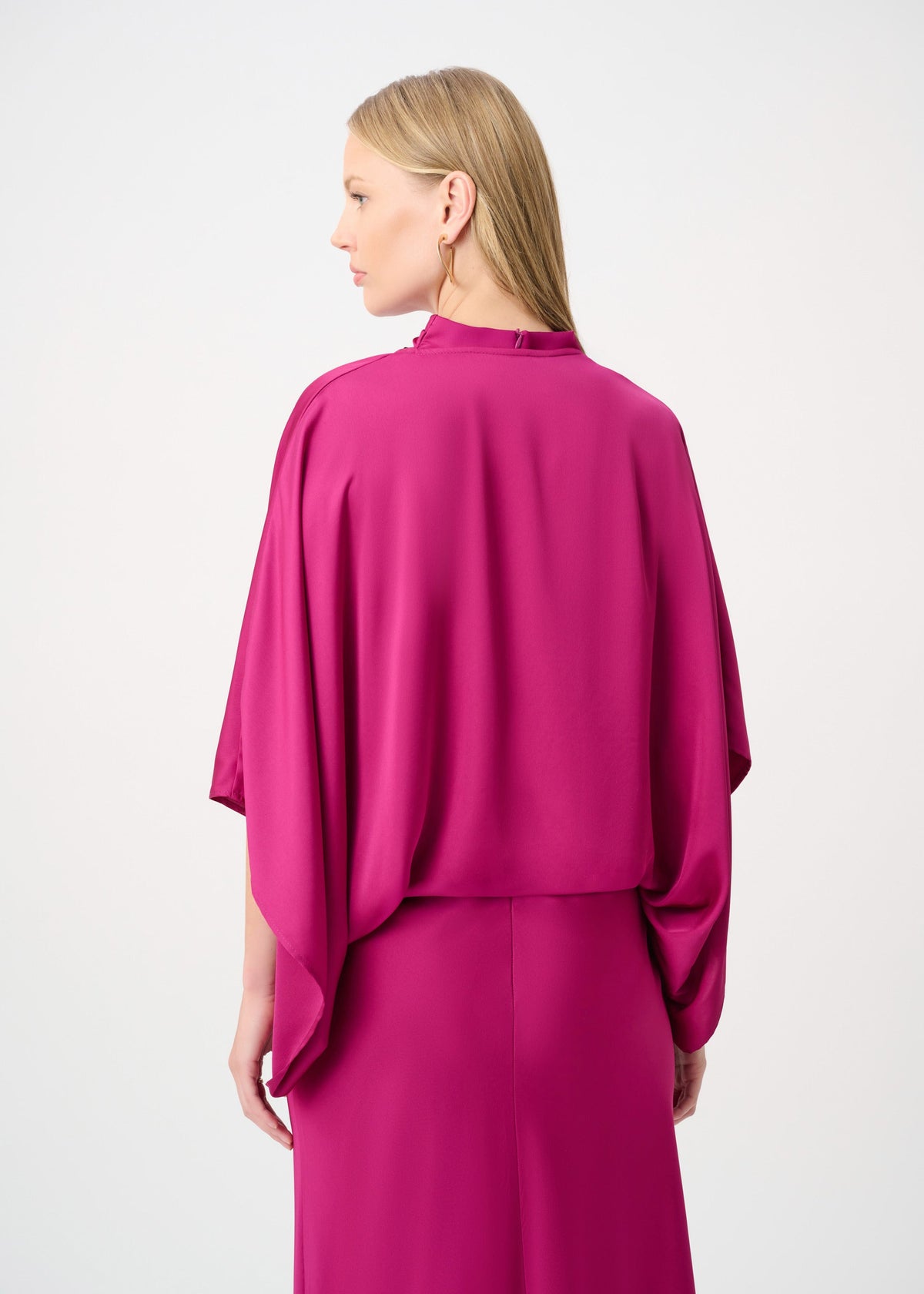 Woman wearing a pink outfit with a cape-like design on a white background