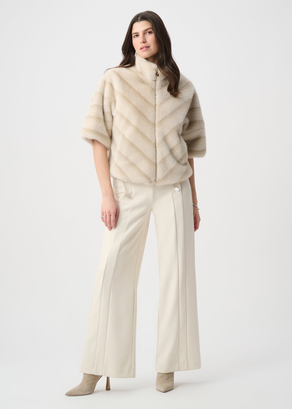 Woman wearing a beige poncho over a white outfit on a white background