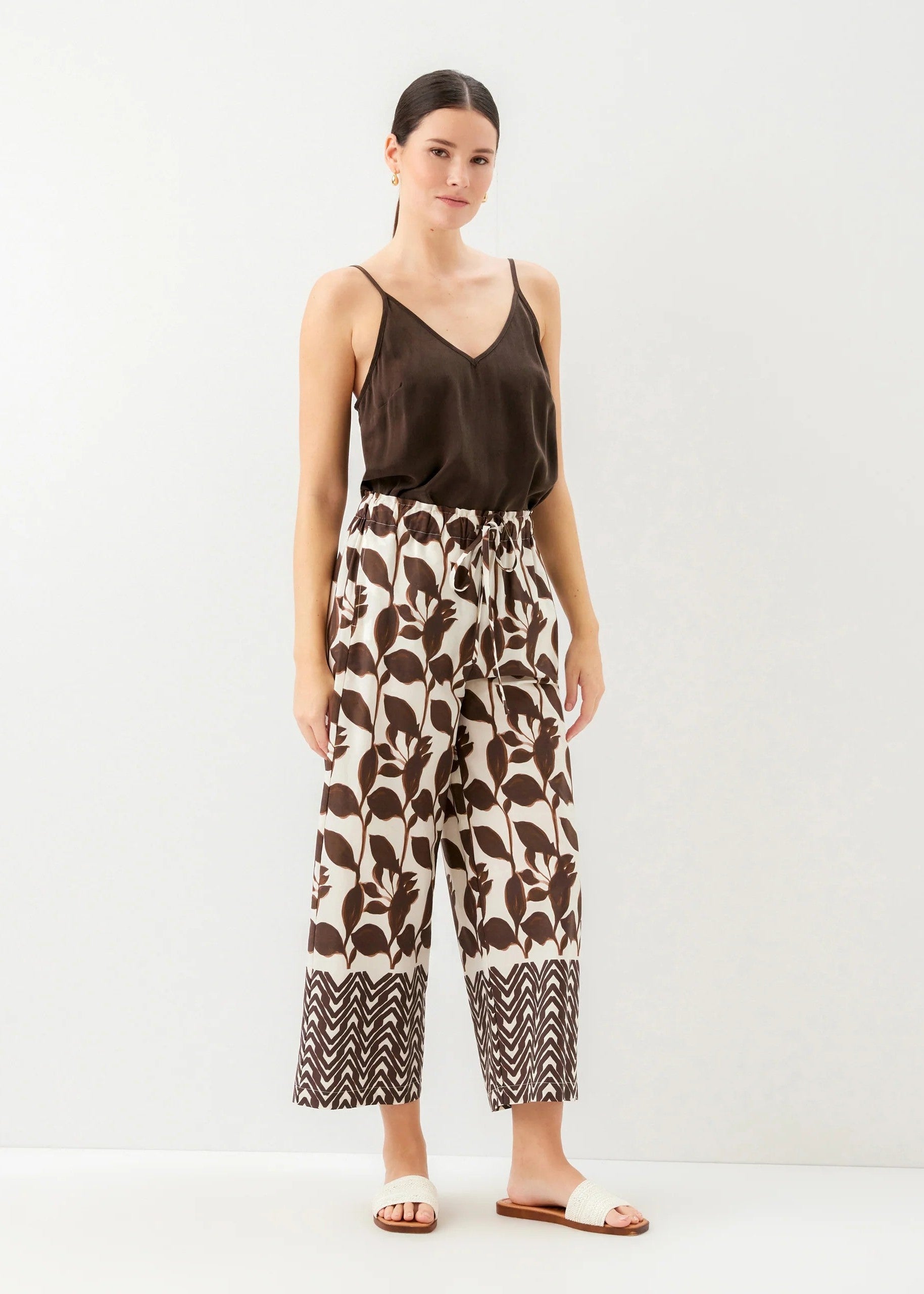 Woman wearing a brown top and patterned pants on a white background