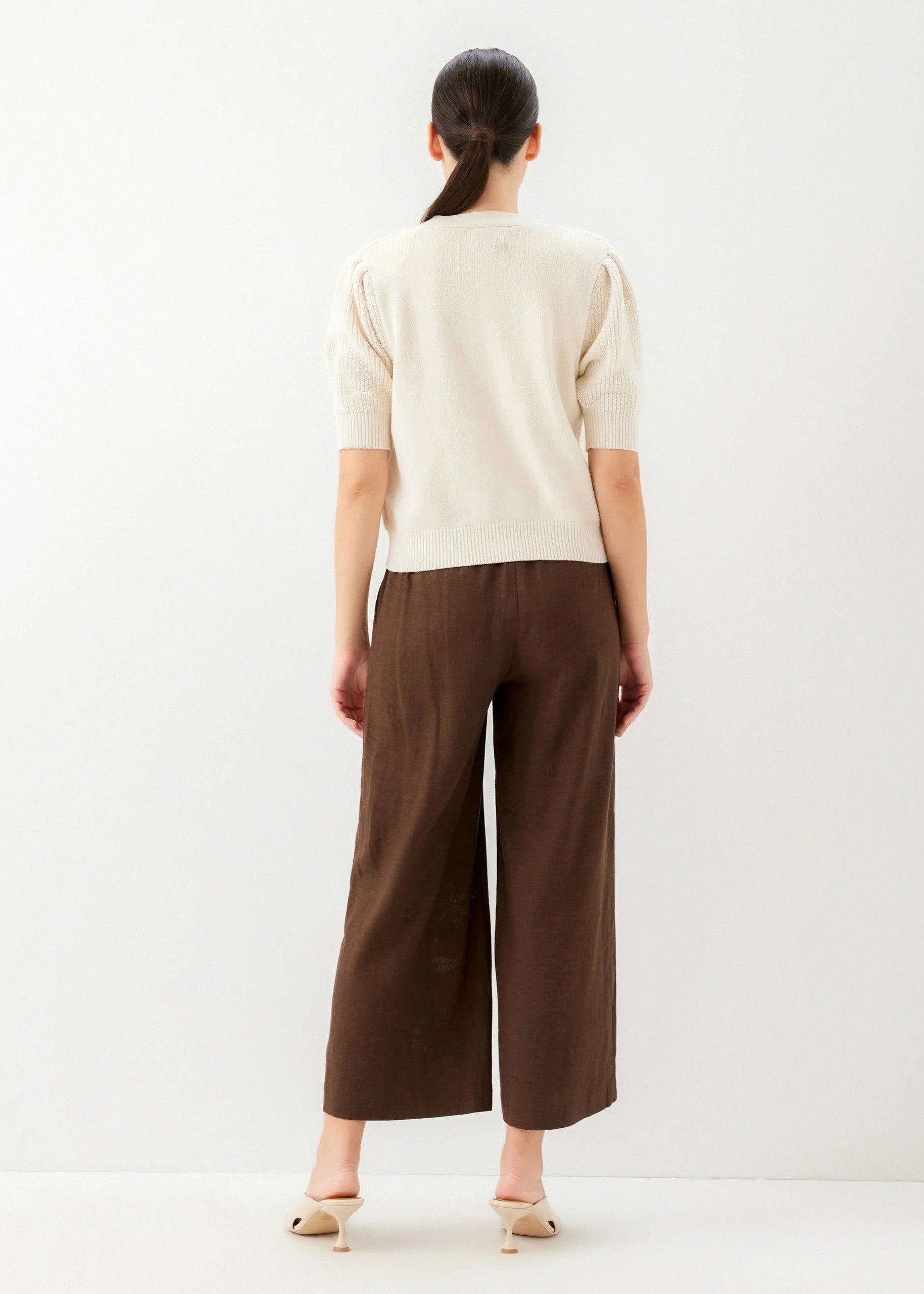 Person wearing a beige top and brown wide-leg pants on a white background