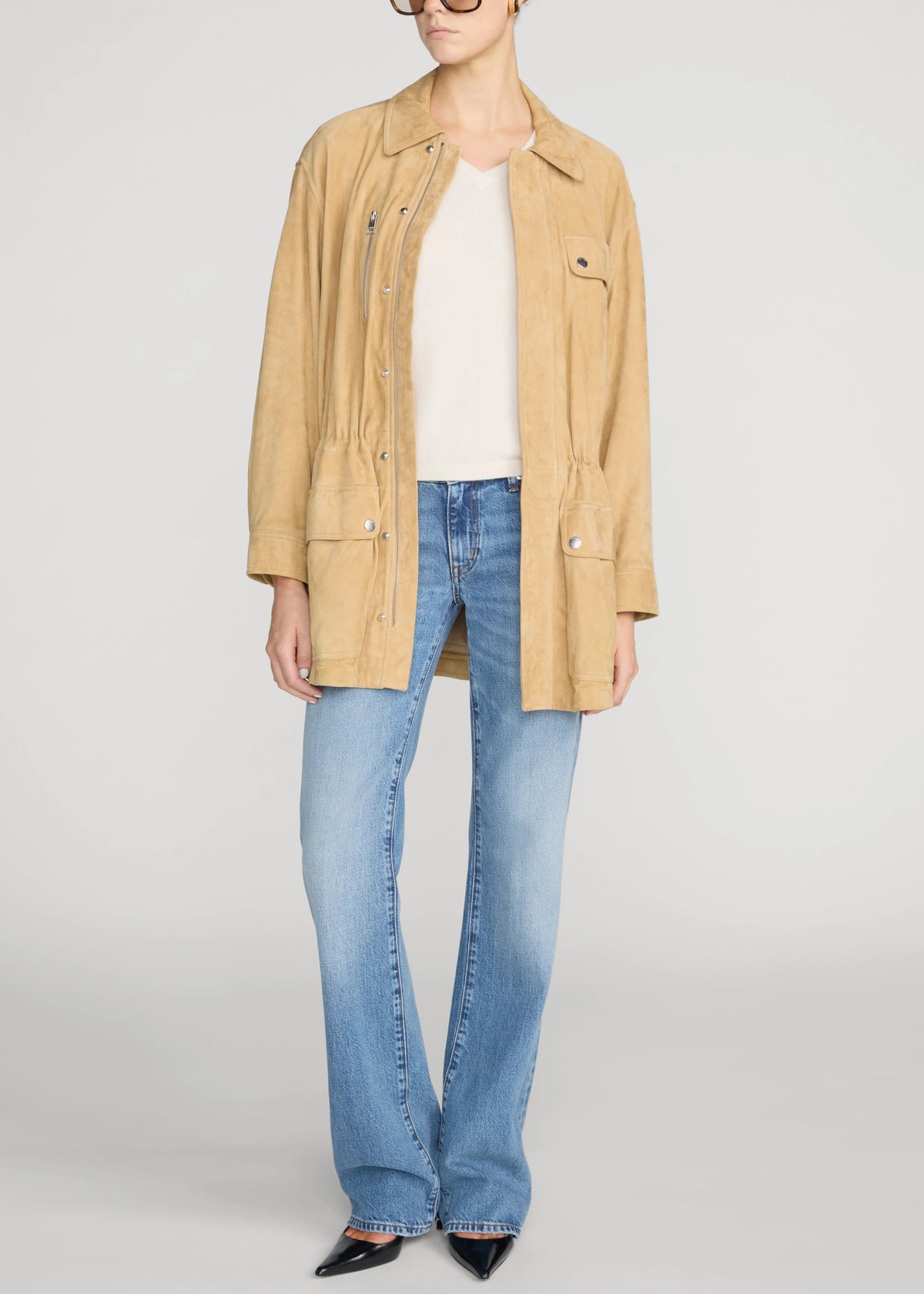 A model wearing a tan corduroy utility jacket over a white top and light blue flare jeans, photographed against a light gray studio background.