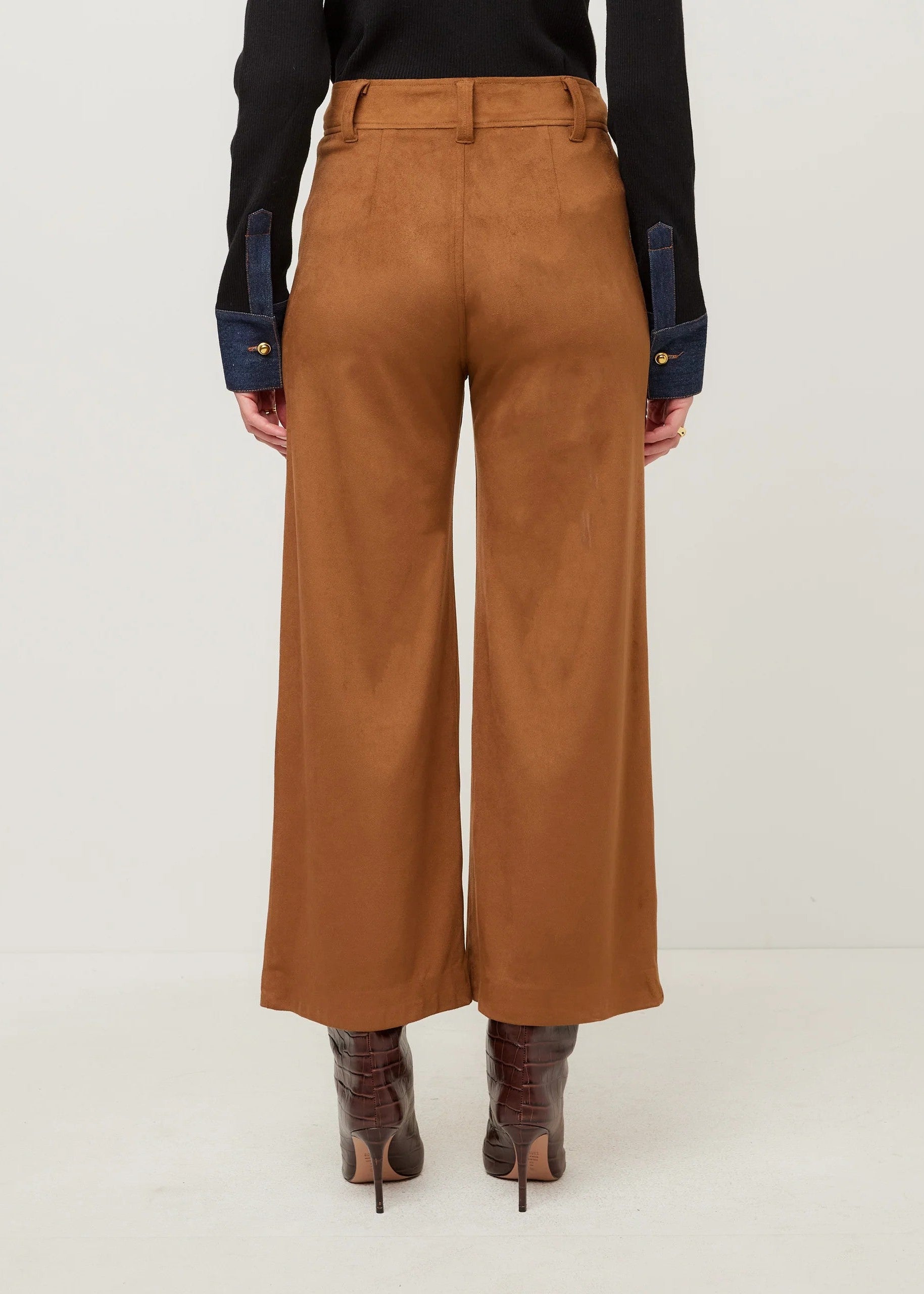 A person shown from the back wearing high-waisted, wide-leg brown pants, a black long-sleeve top with dark blue contrast cuffs, and brown heeled boots against a plain light background.