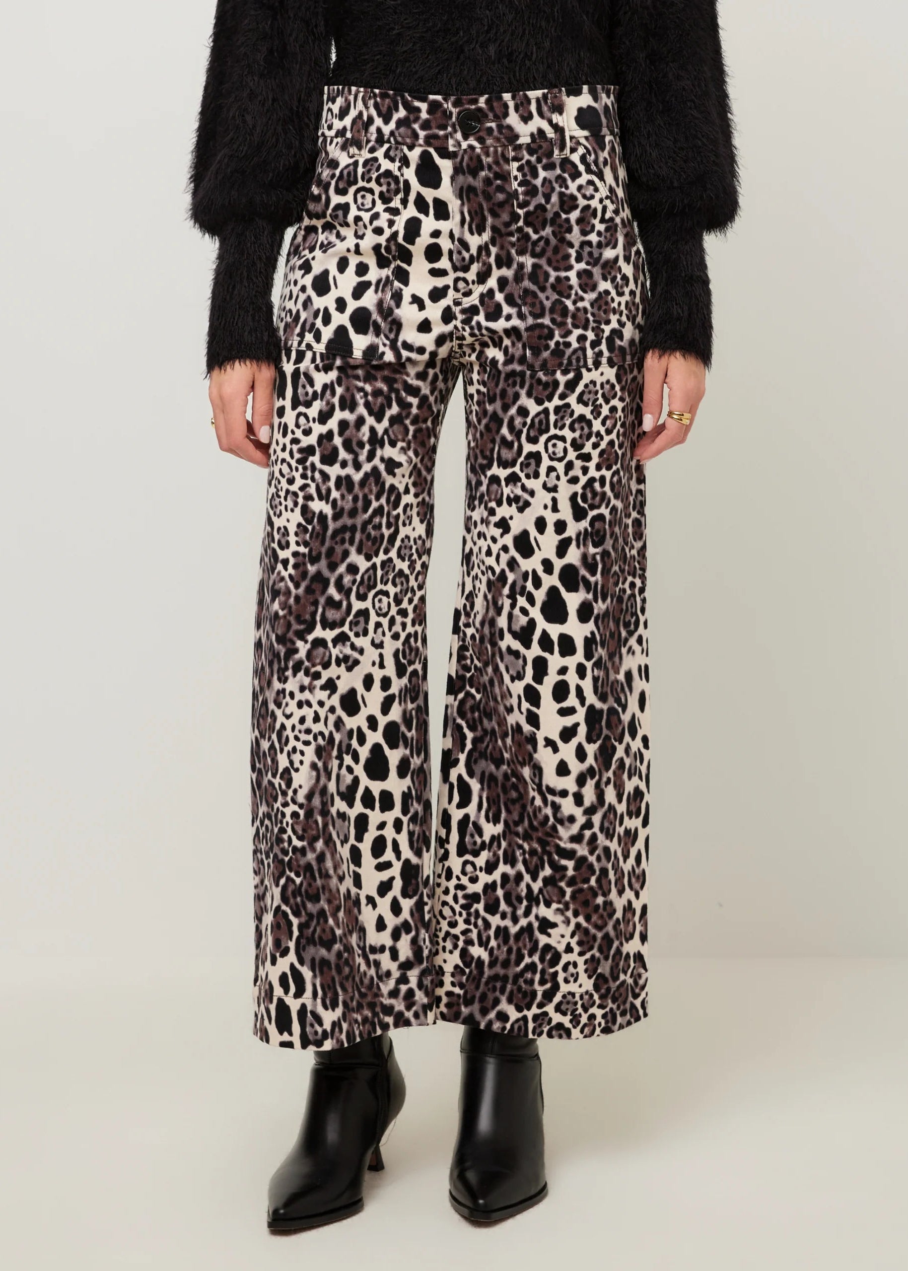 A model wearing high-waisted, wide-leg trousers with a brown, black, and beige leopard print, styled with a black fuzzy sweater and black pointed-toe ankle boots.