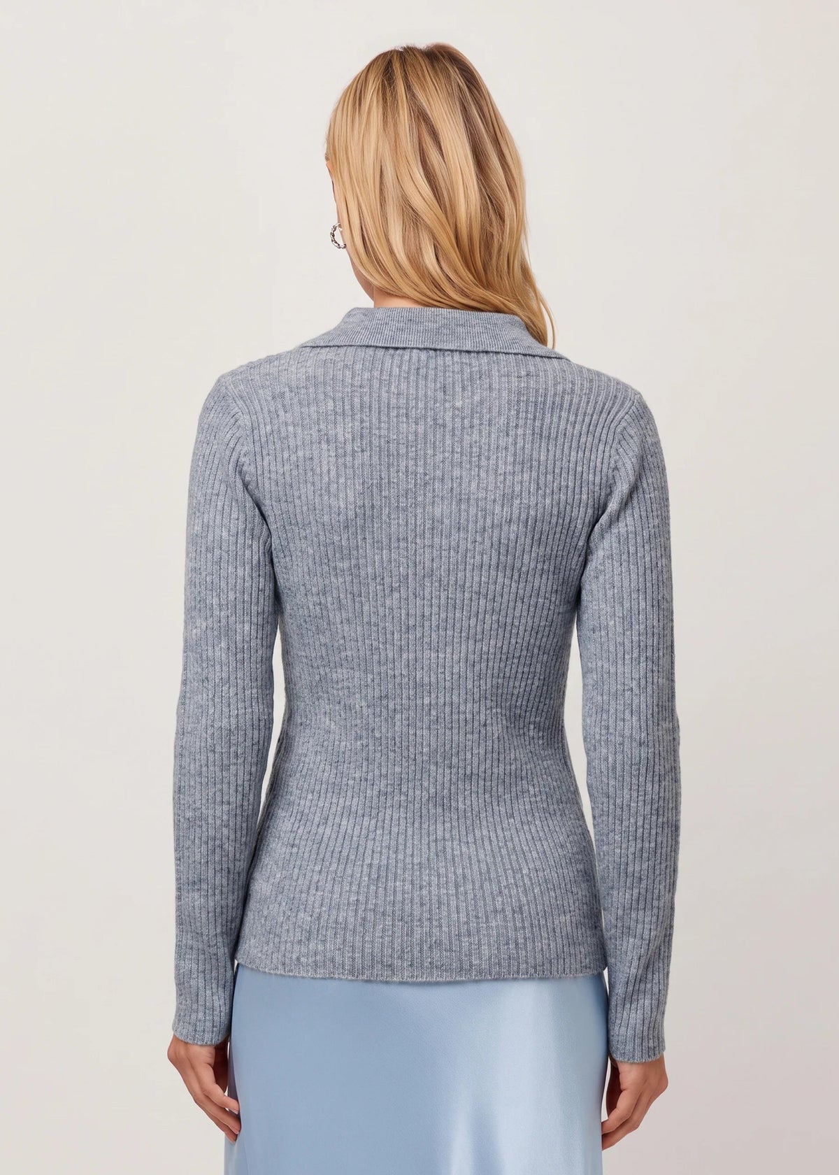 A woman shown from the back wearing a ribbed knit long-sleeve top in heather gray, paired with a light blue skirt, against a plain light beige studio background.