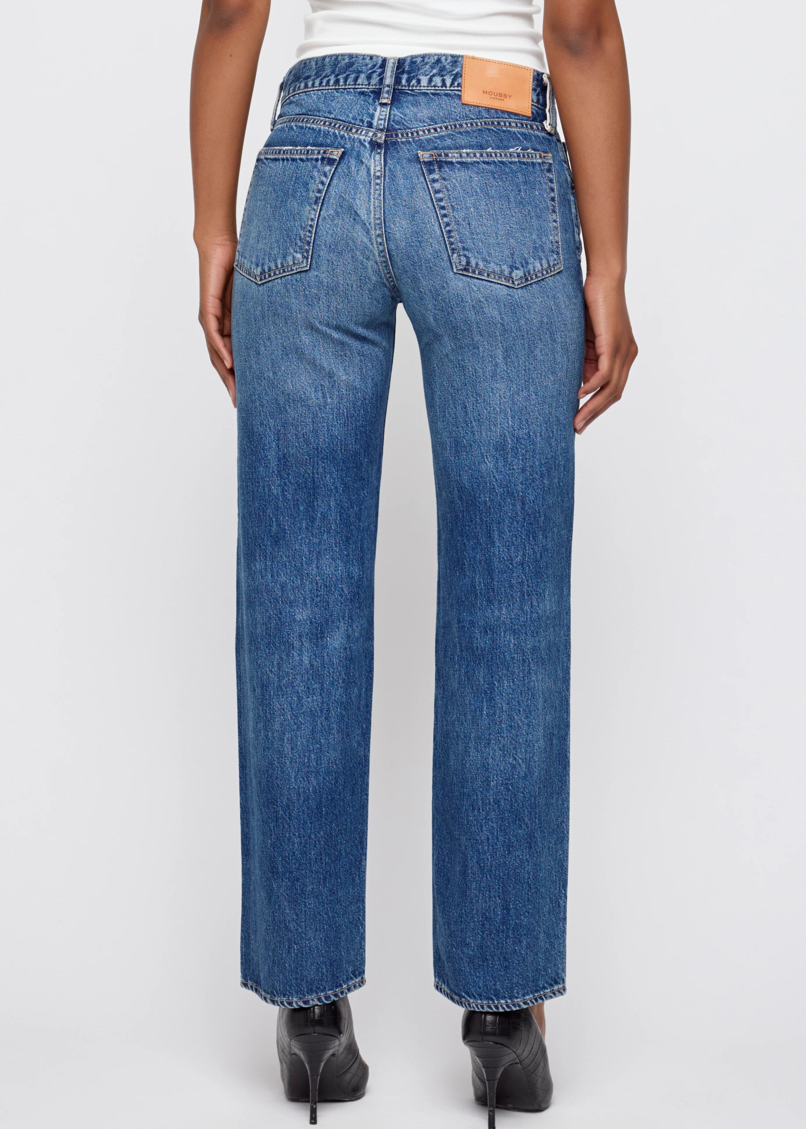 Person wearing blue jeans and black high heels on a white background