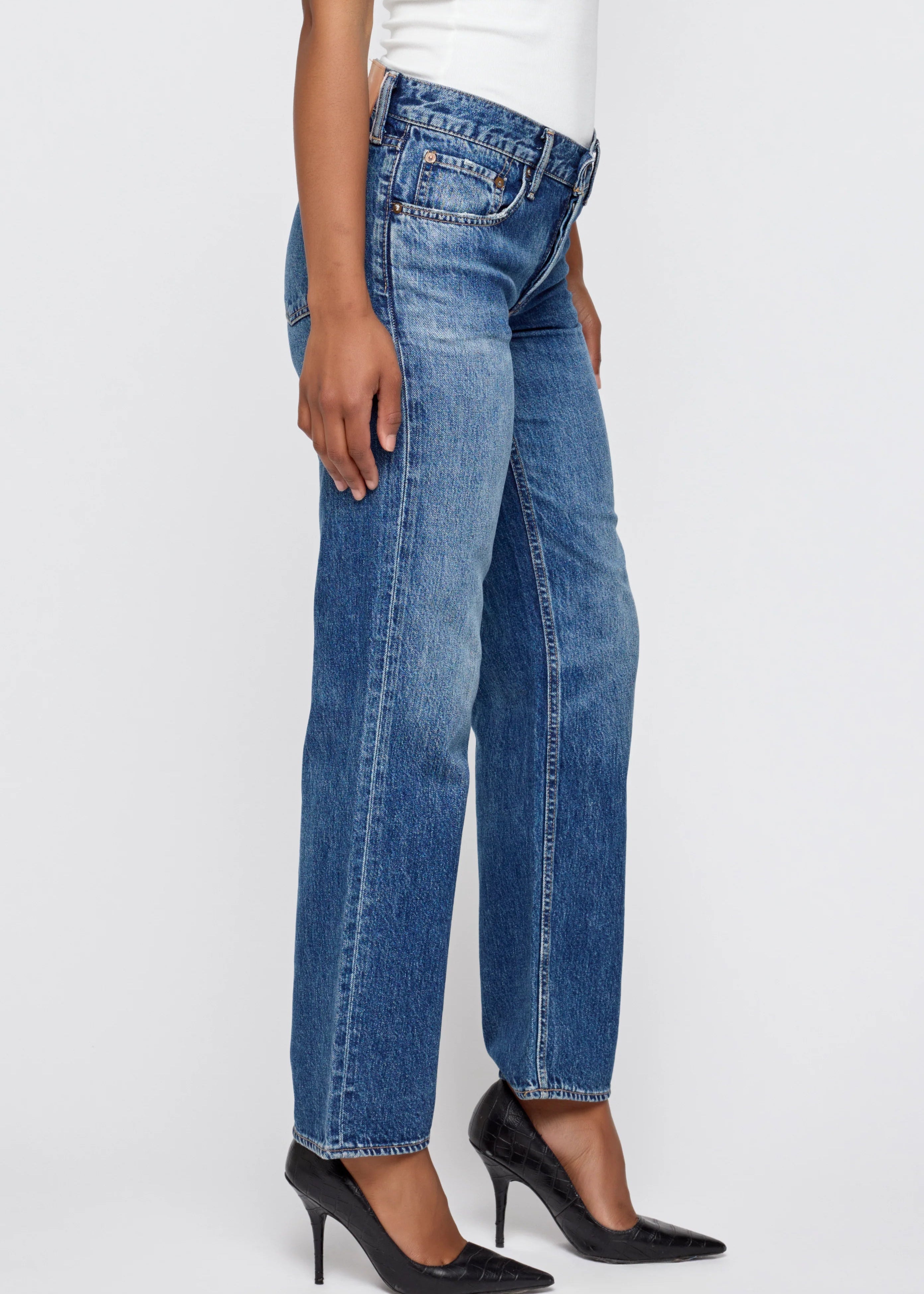 Person wearing blue jeans and black high heels on a white background