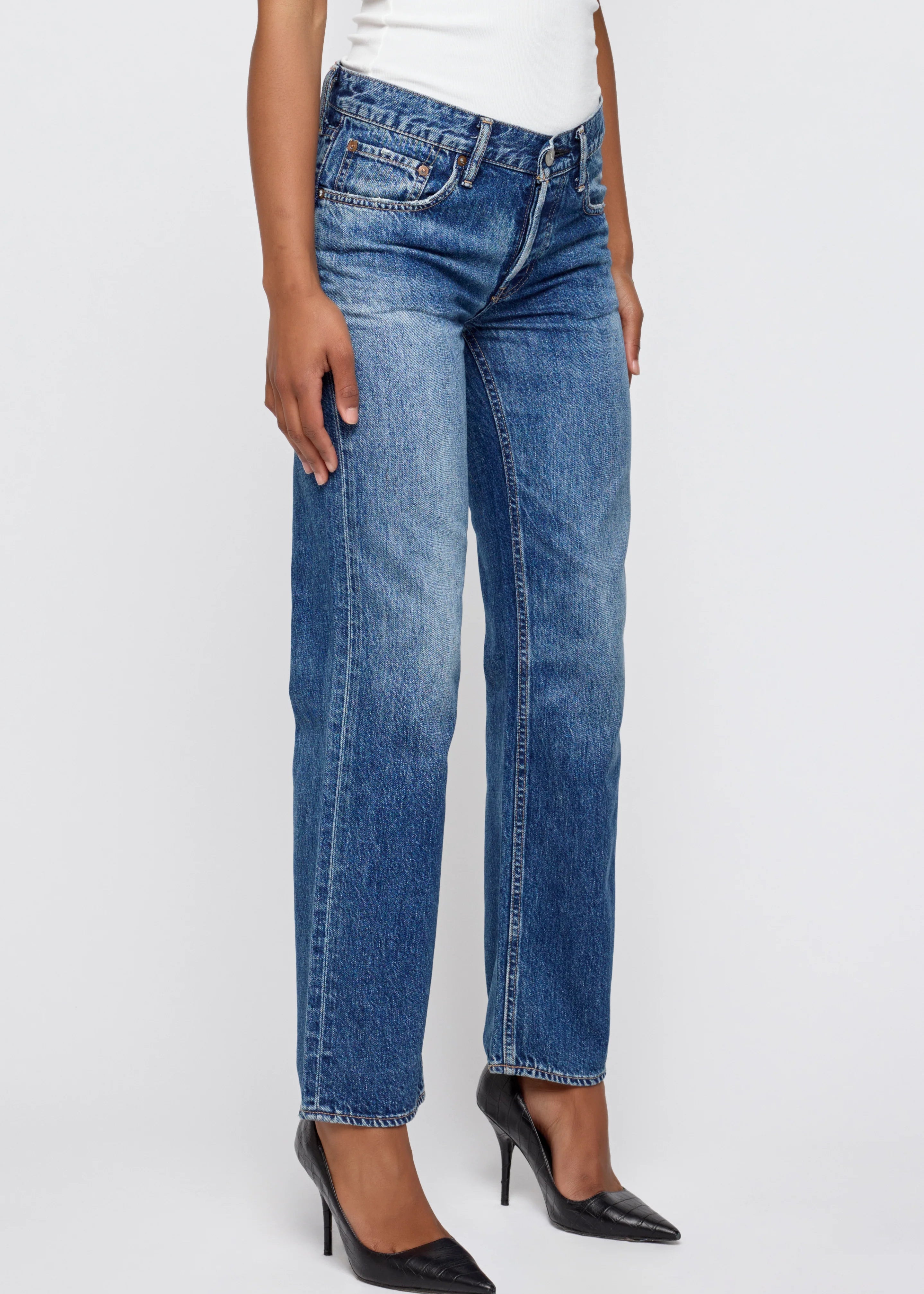 Person wearing blue jeans and black high heels on a white background