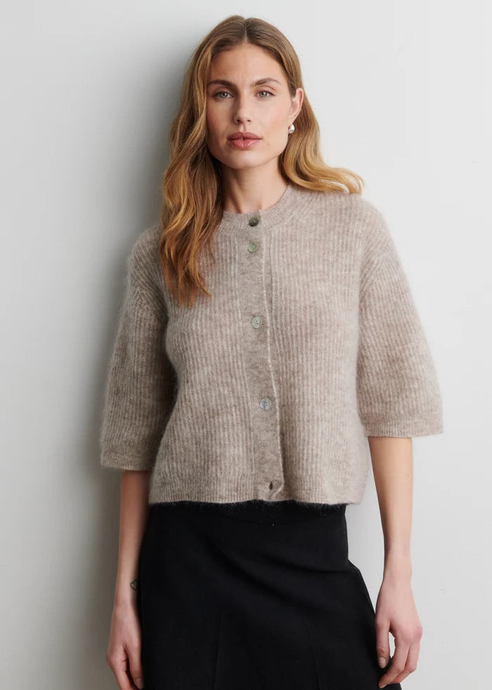Woman wearing a beige knitted cardigan against a plain background