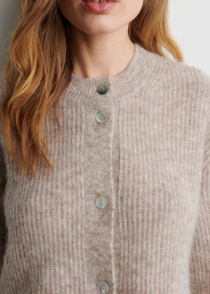 Close-up of a person wearing a beige knitted cardigan with buttons.