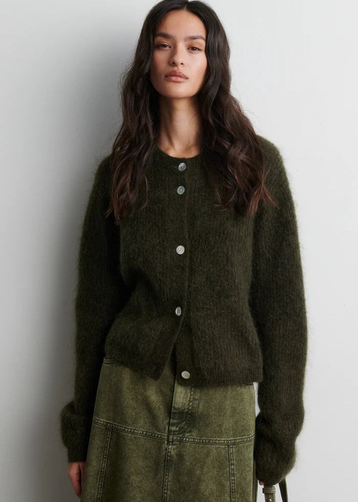 Woman wearing a dark green cardigan against a plain background