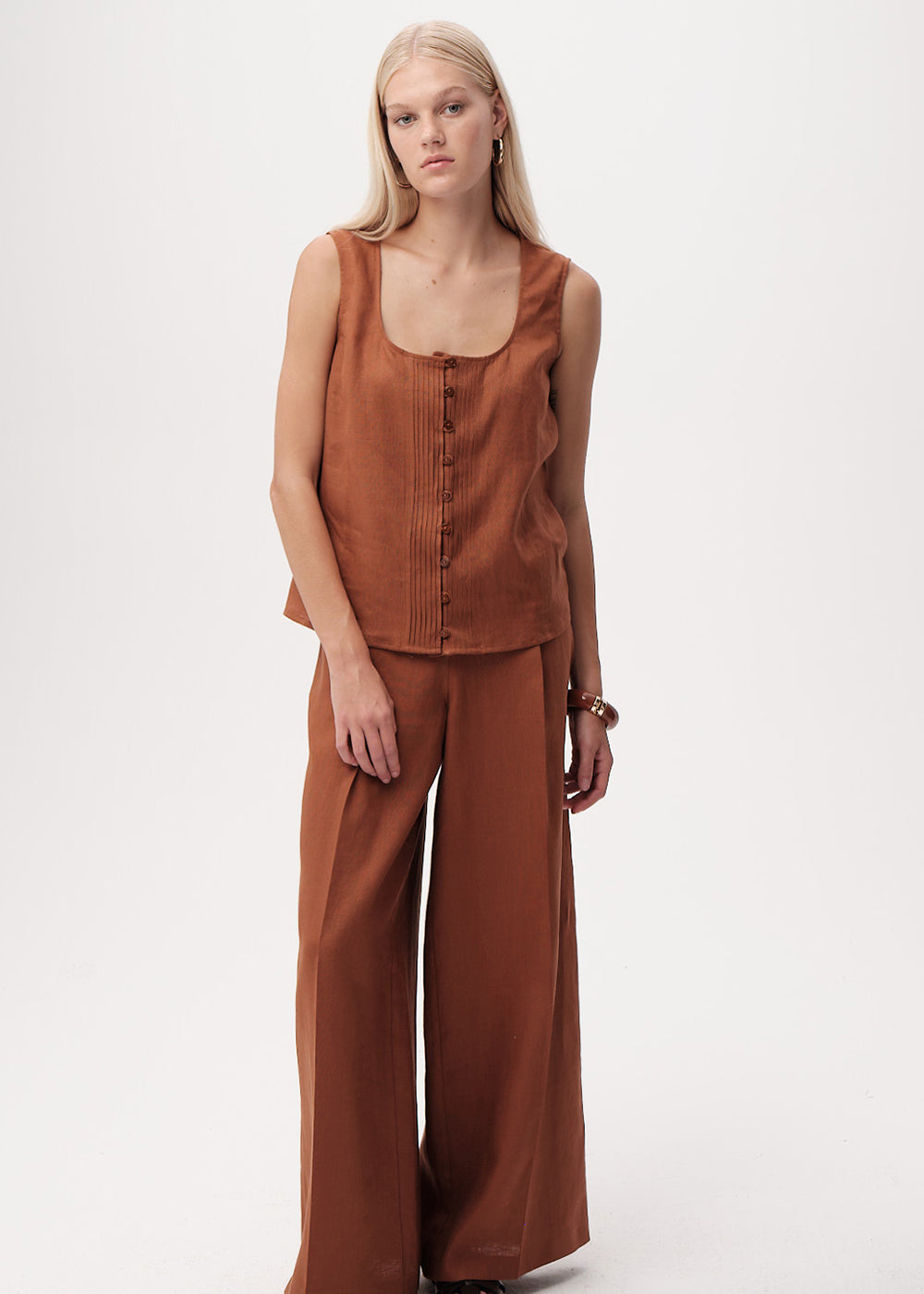 Woman wearing a brown sleeveless top and wide-leg pants on a white background